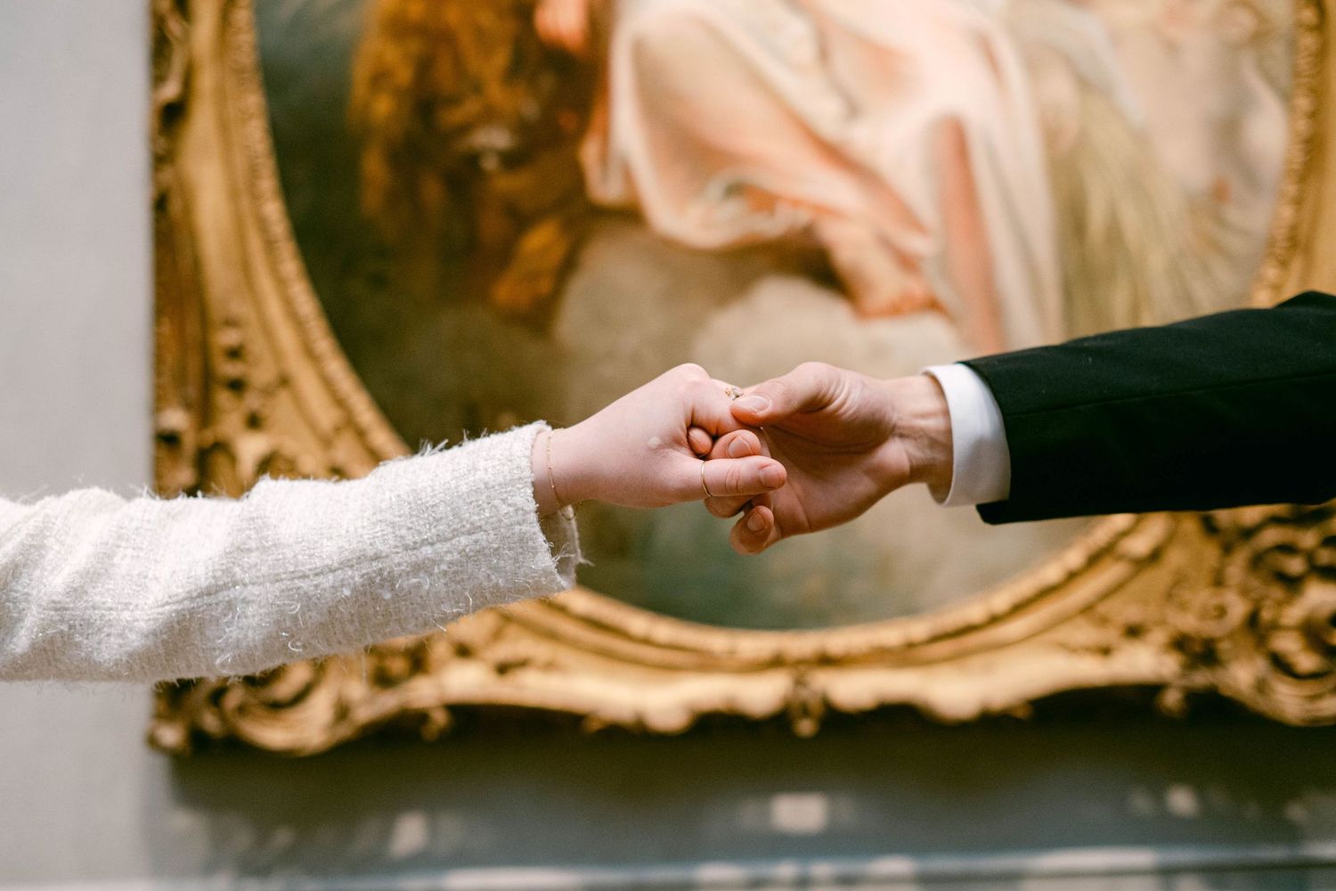 Hands holding a white lace wedding dress against an ornate gold frame background.