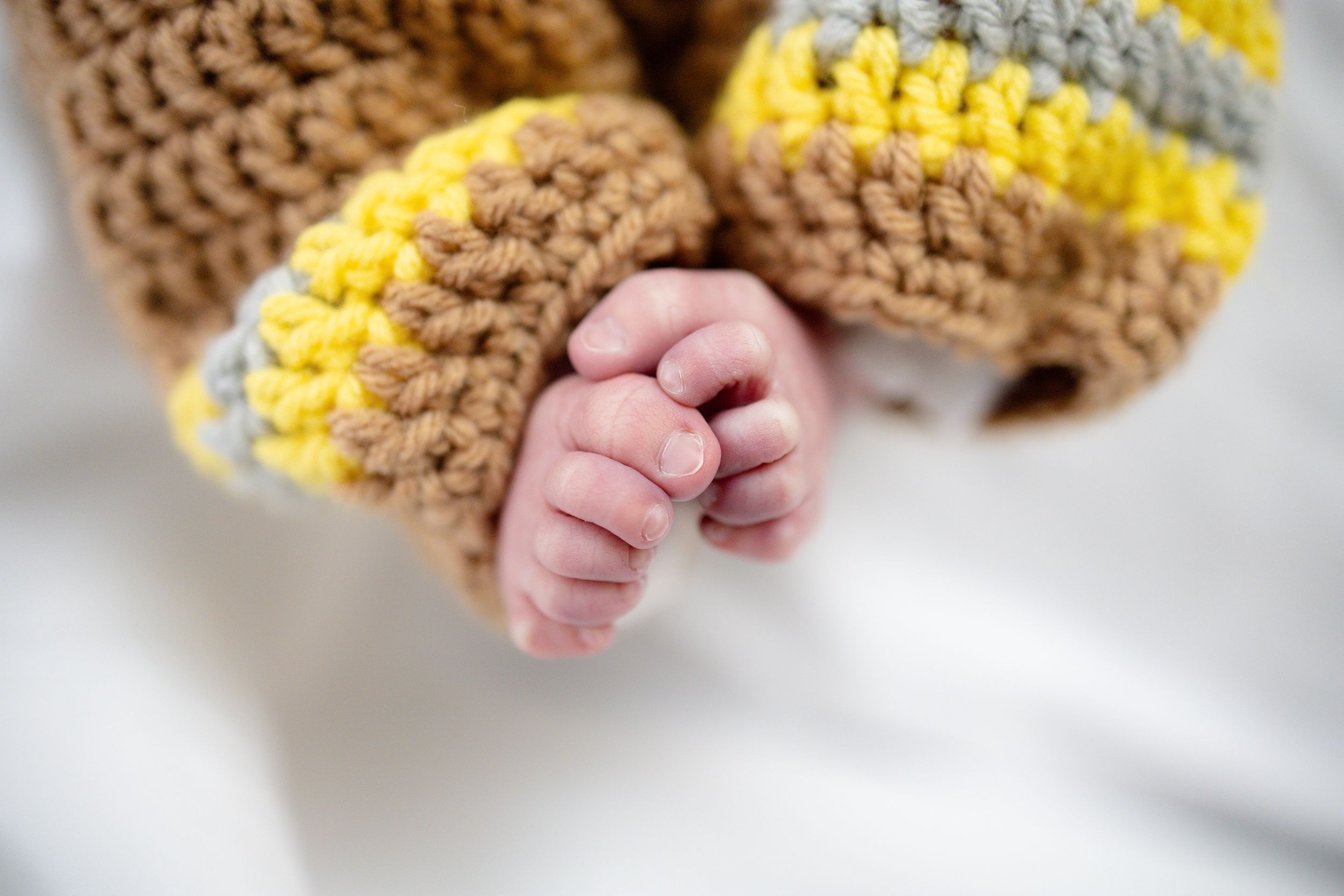 Close-up of a newborn baby's tiny hands in a brown, yellow, and gray striped crochet outfit.