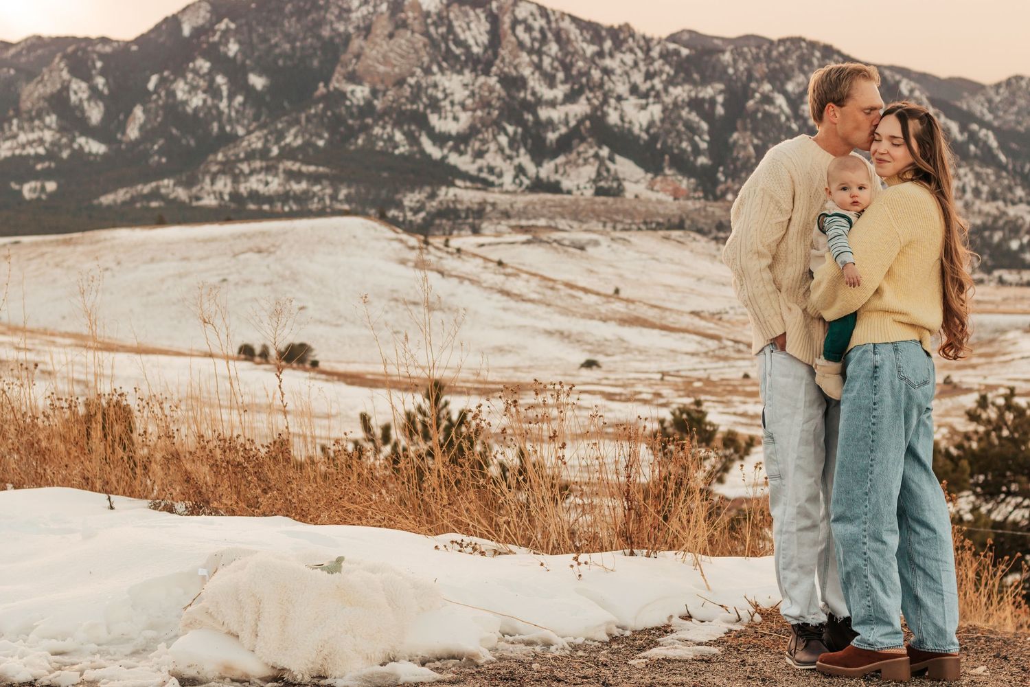 Couple in denim embracing in a snowy winter field during golden hour at sunset |Best Family Photo Location with Mountain Views