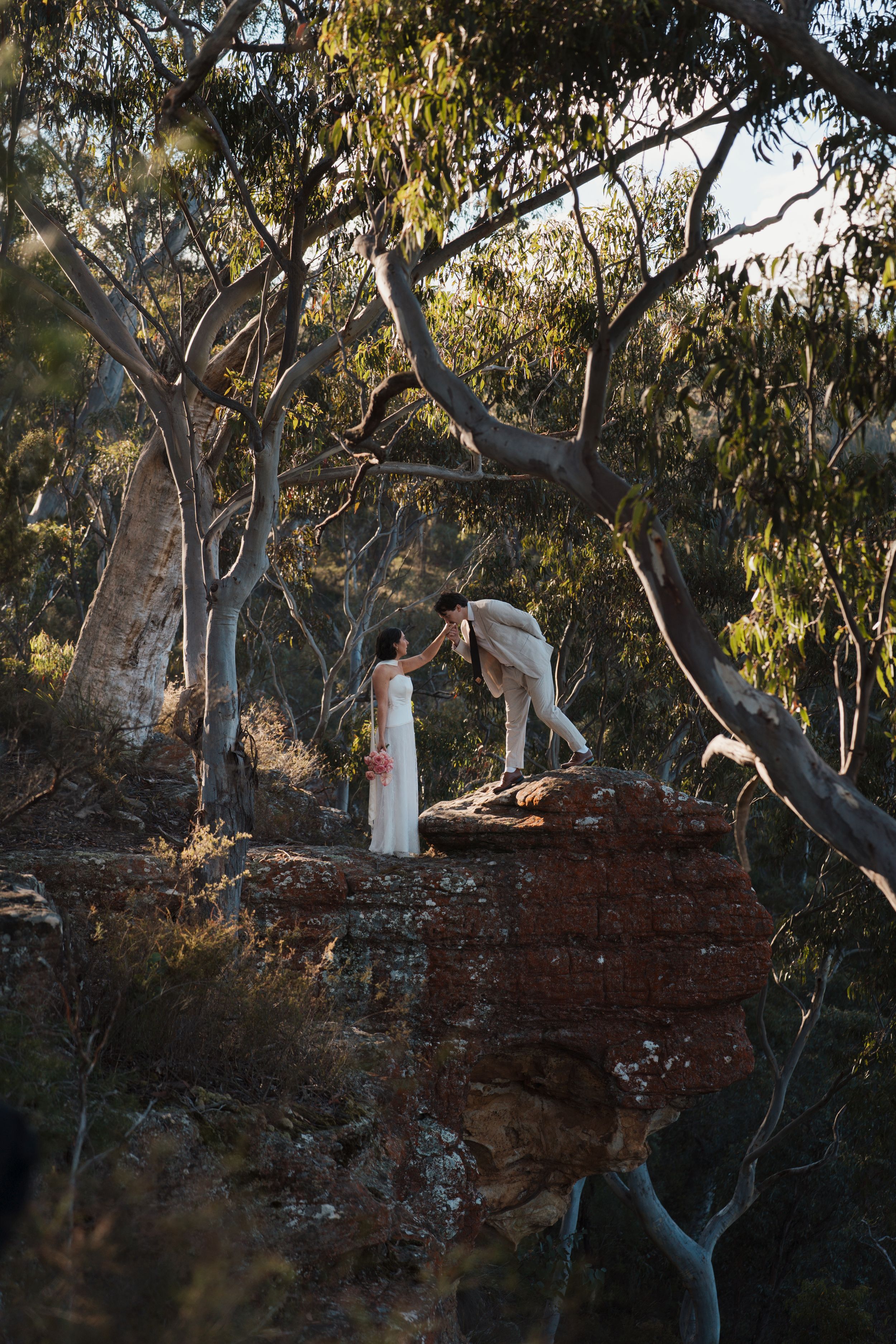 Bride and groom share a romantic moment on a rocky outcrop surrounded by Australian bush eucalyptus trees at golden hour elopement