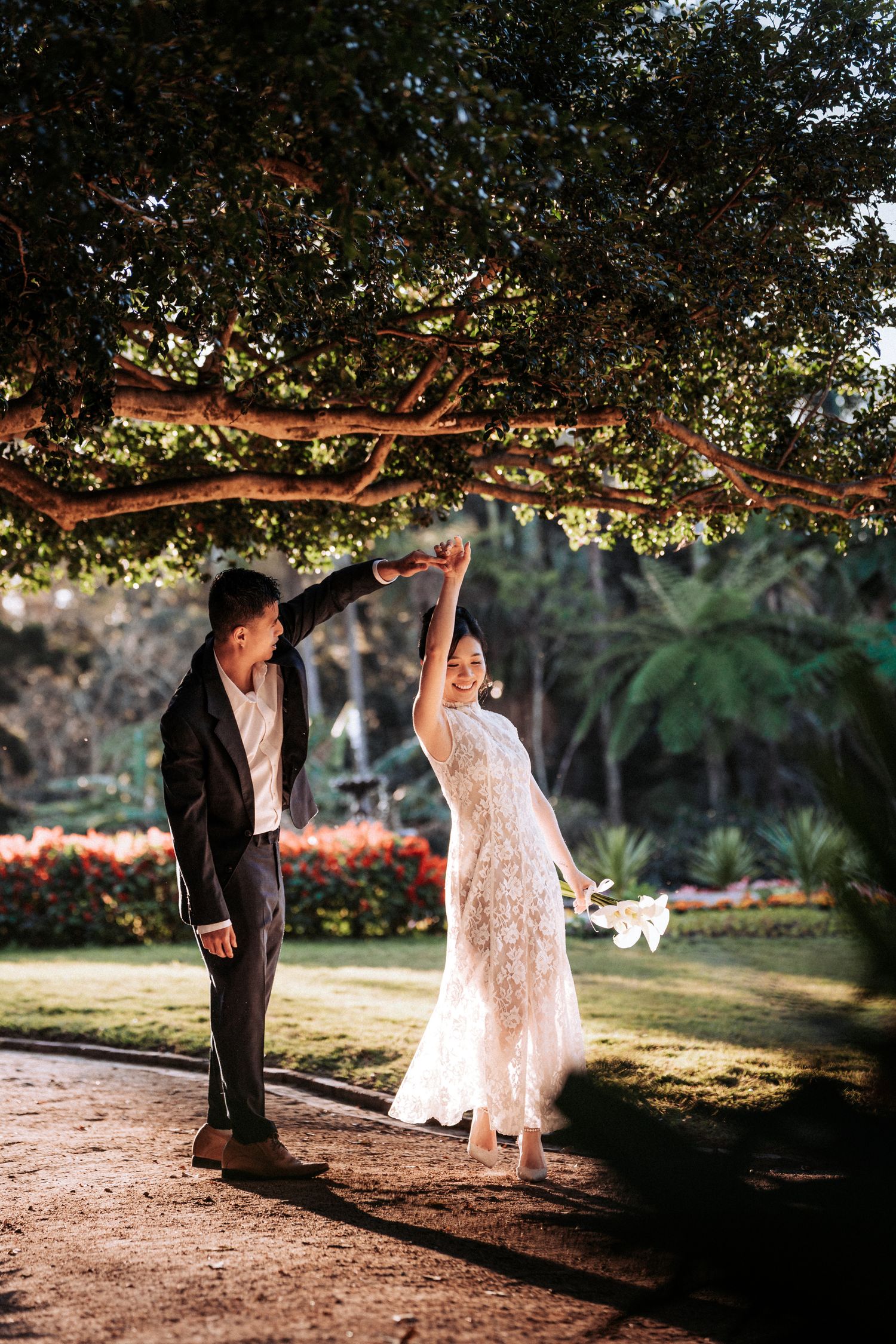 Bride and groom dancing under a large tree in a lush garden, bride in lace gown twirling gracefully.