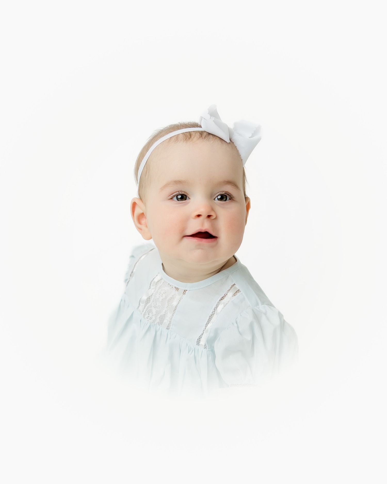 Portrait of infant wearing white dress and bow headband.