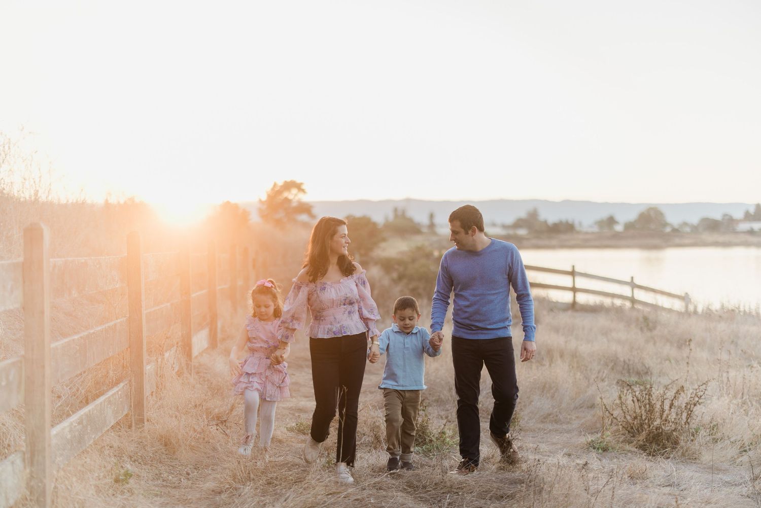 Family walks together along waterfront path during golden hour.
