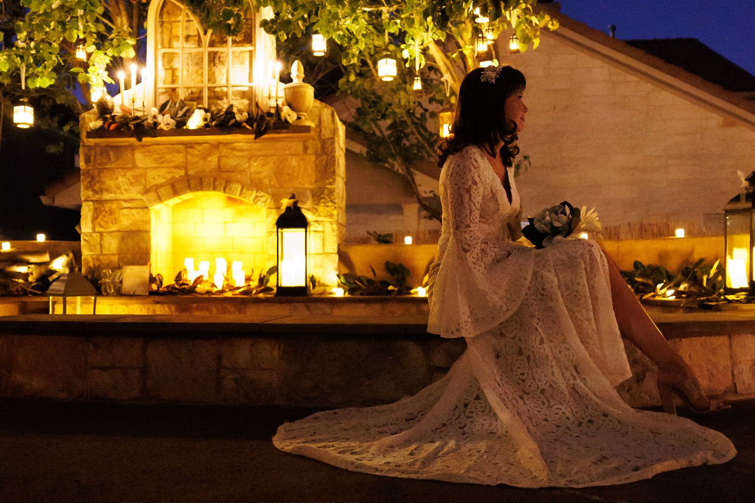 Silhouette of bride in lace dress sitting by illuminated courtyard at night.