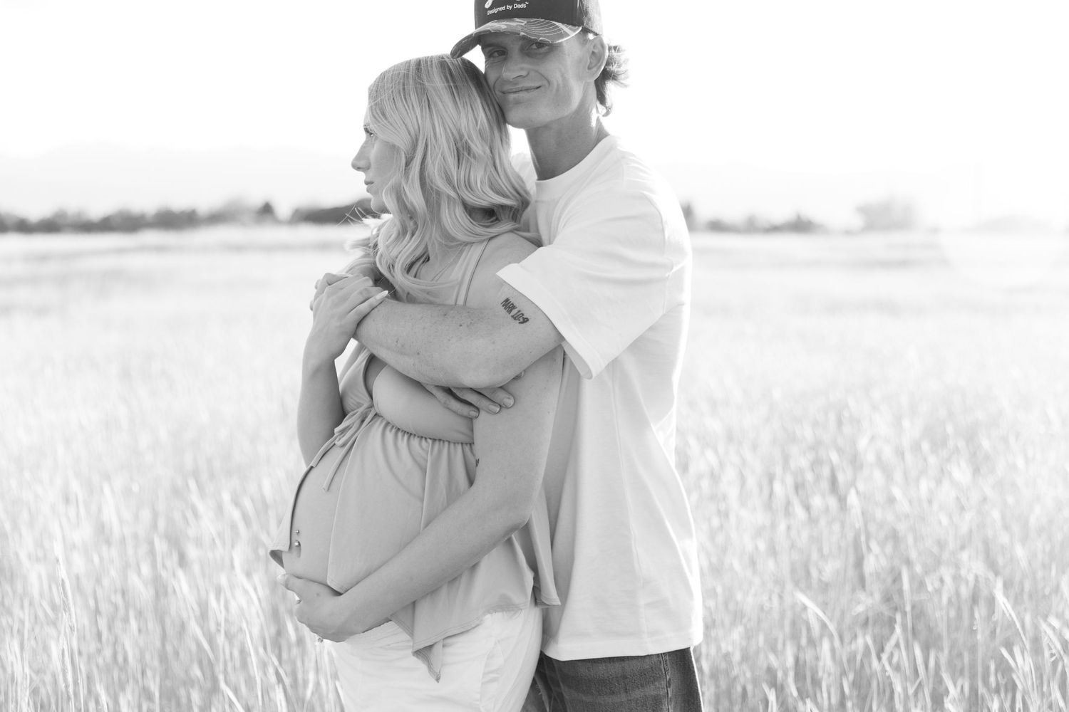 Black and white photo of couple embracing in a sunlit golden grain field.