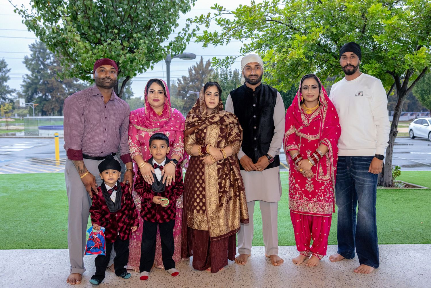 Family of seven in traditional South Asian attire, including turbans and embroidered shawls, posing together on a lawn in a park.