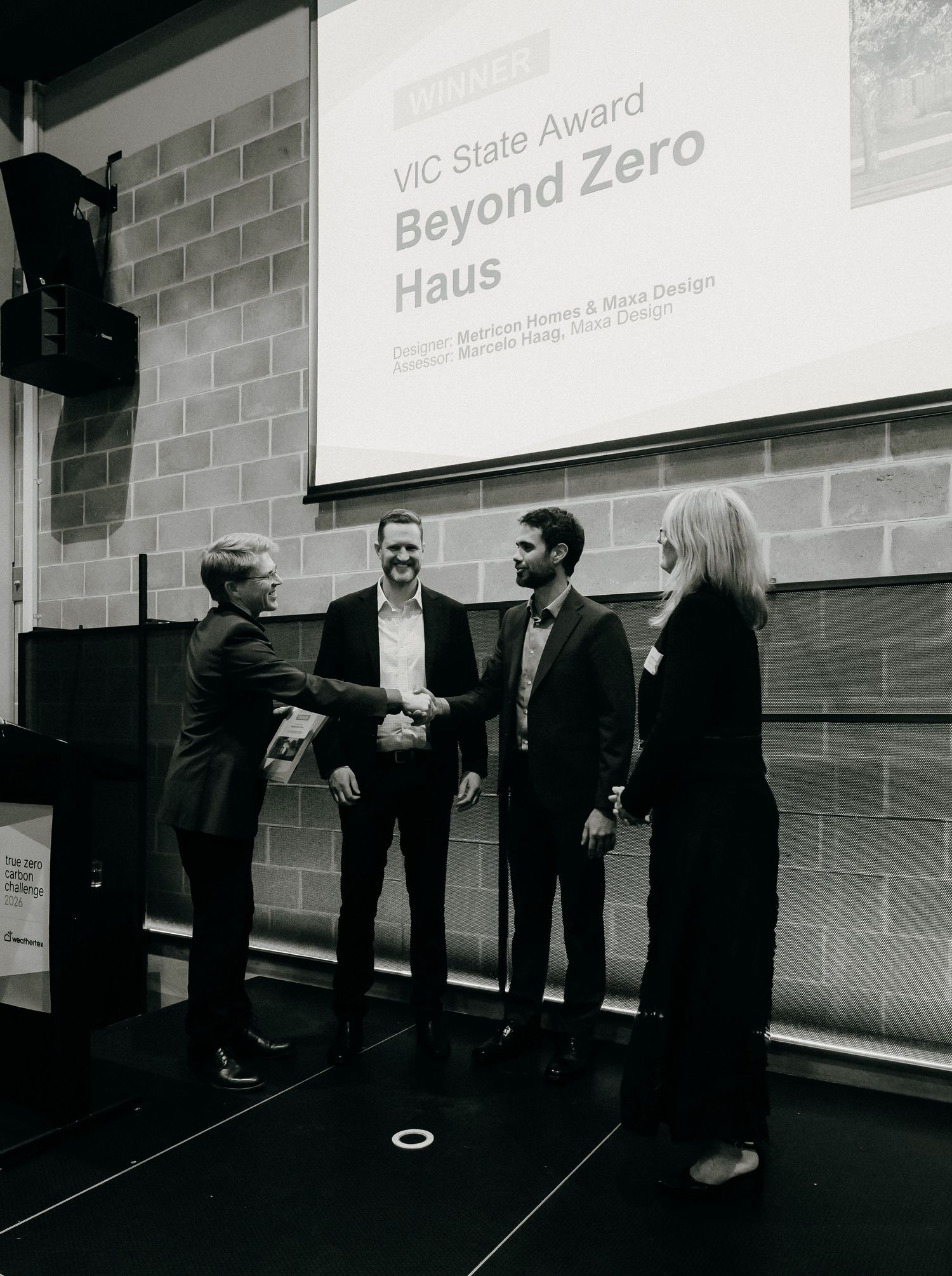 Award ceremony for Beyond Zero Haus VIC State Award, with four professionals shaking hands on stage.