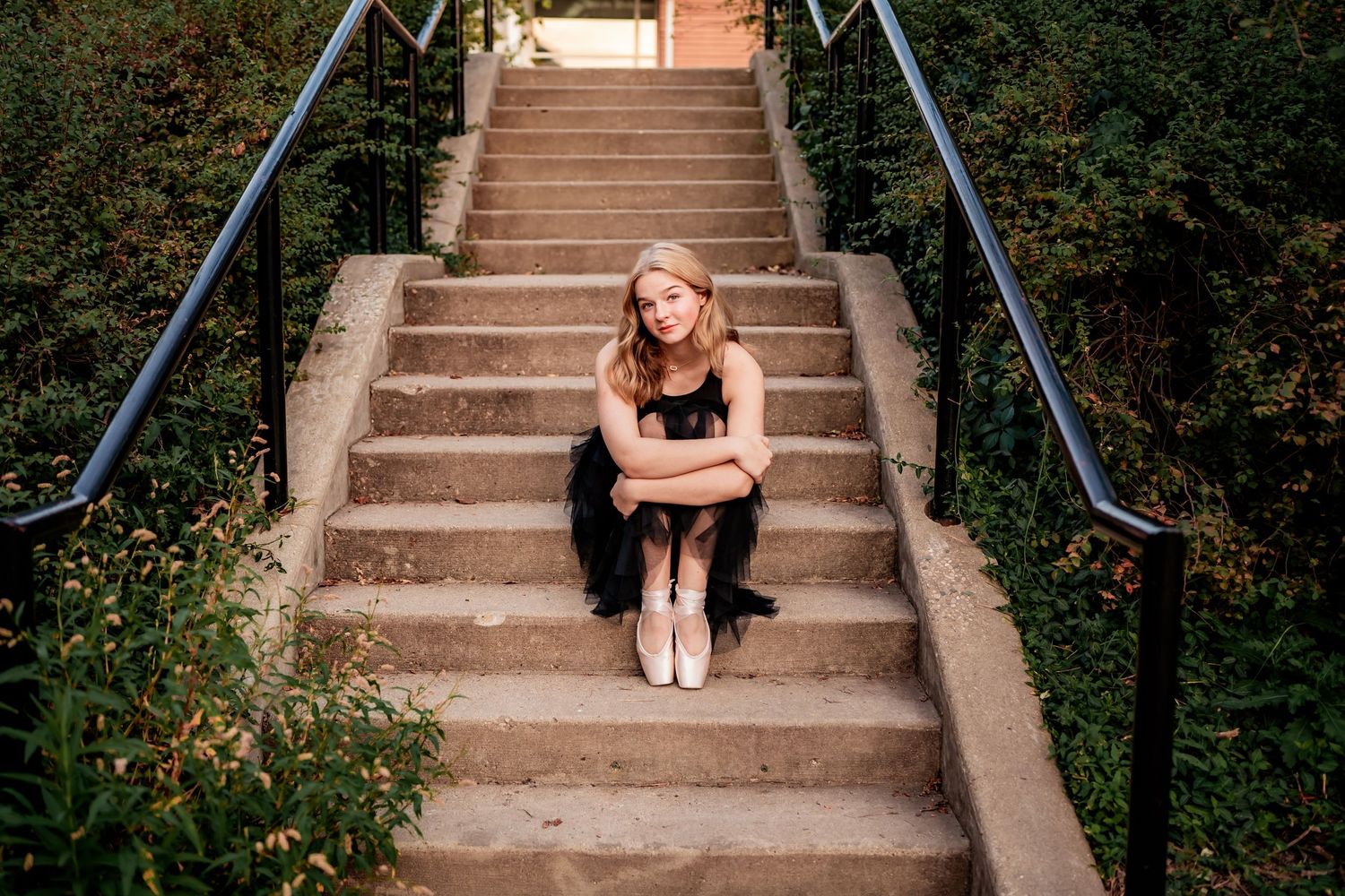 Ballet dancer in casual wear sits thoughtfully on outdoor concrete steps.