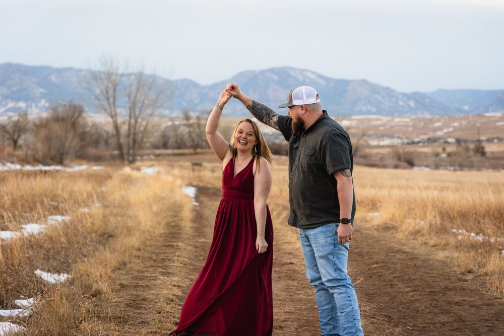 A couple dances together on a dirt path with mountains and dry grass in the background during winter.