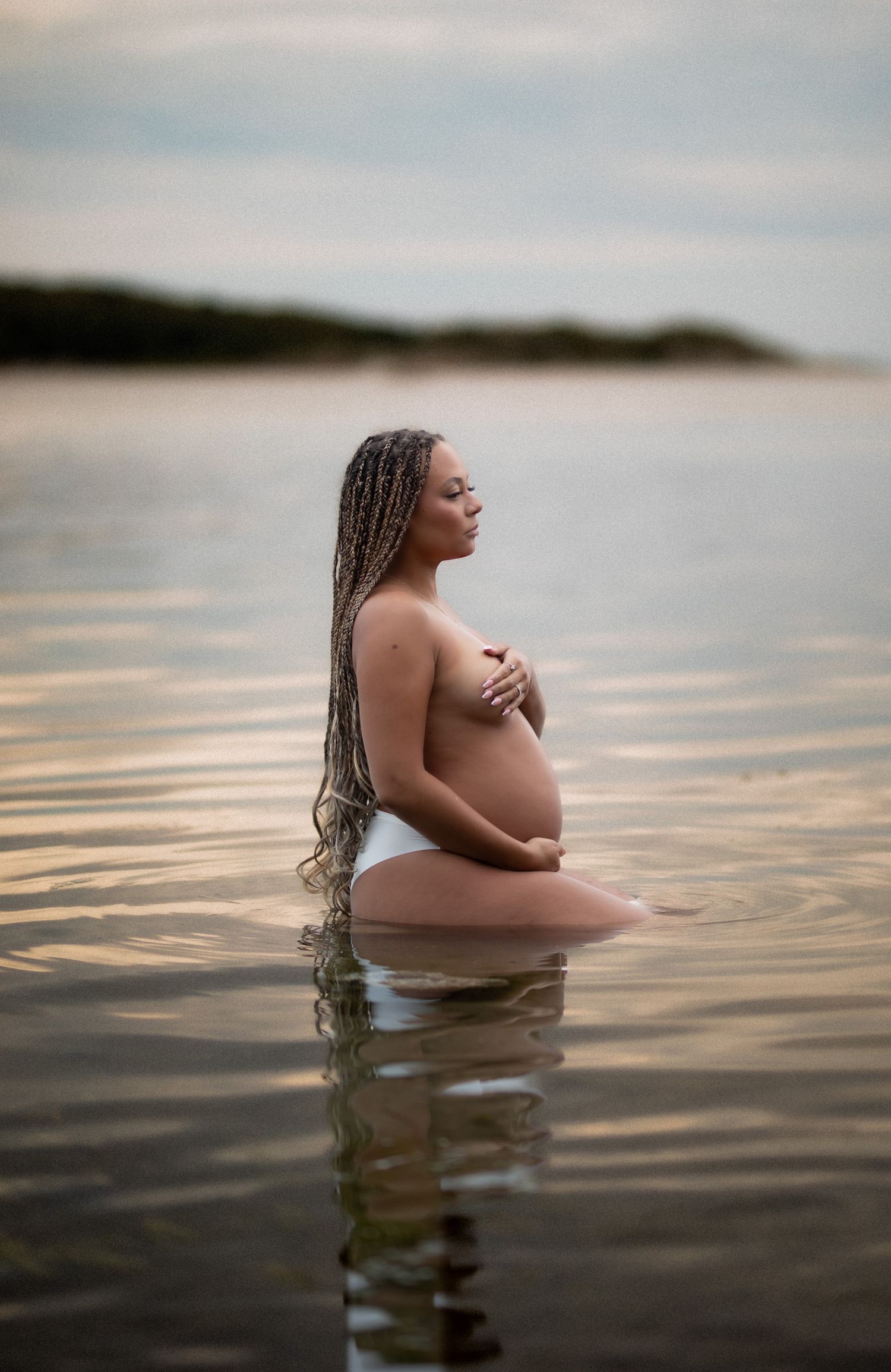 gravid kvinna står i vattnet och kollar bortåt. hon håller om sin gravidmage.