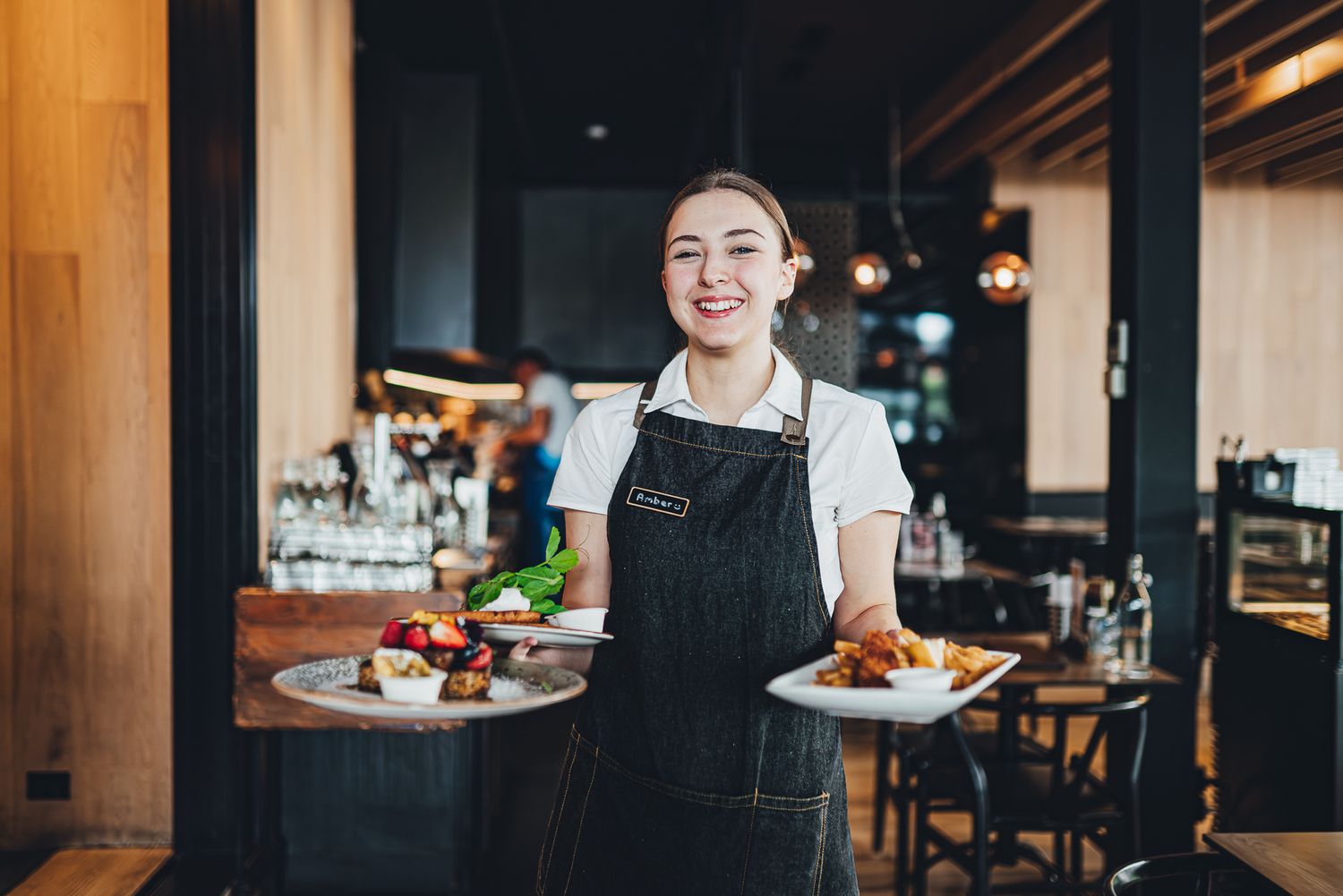 Server in black apron carrying plates of food in Melbourne restaurant during a professional branding and commercial photoshoot.