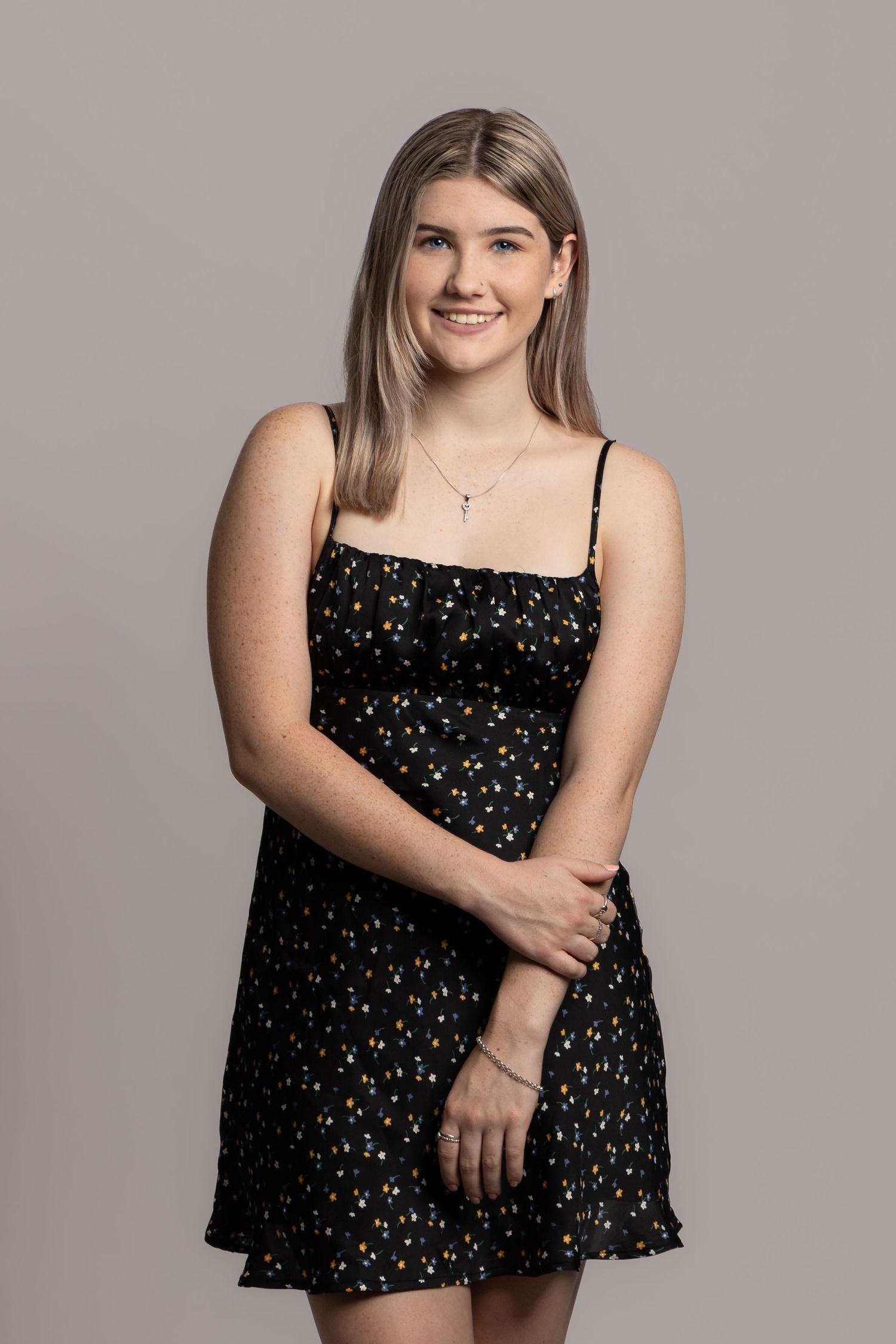 Studio portrait of someone in a black floral mini dress with spaghetti straps against a neutral background.