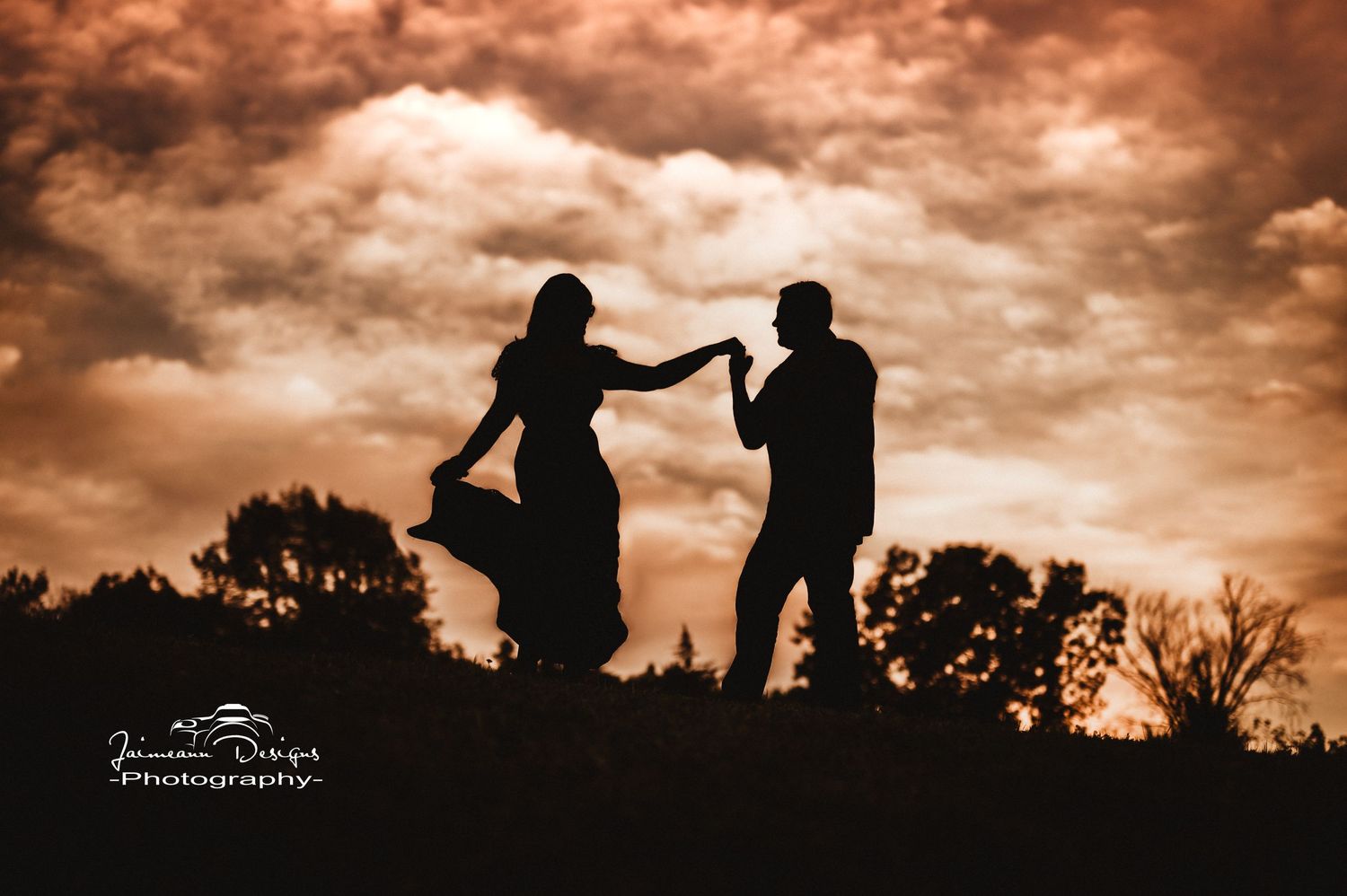Dramatic silhouette of dancing couple against orange sunset sky with clouds.