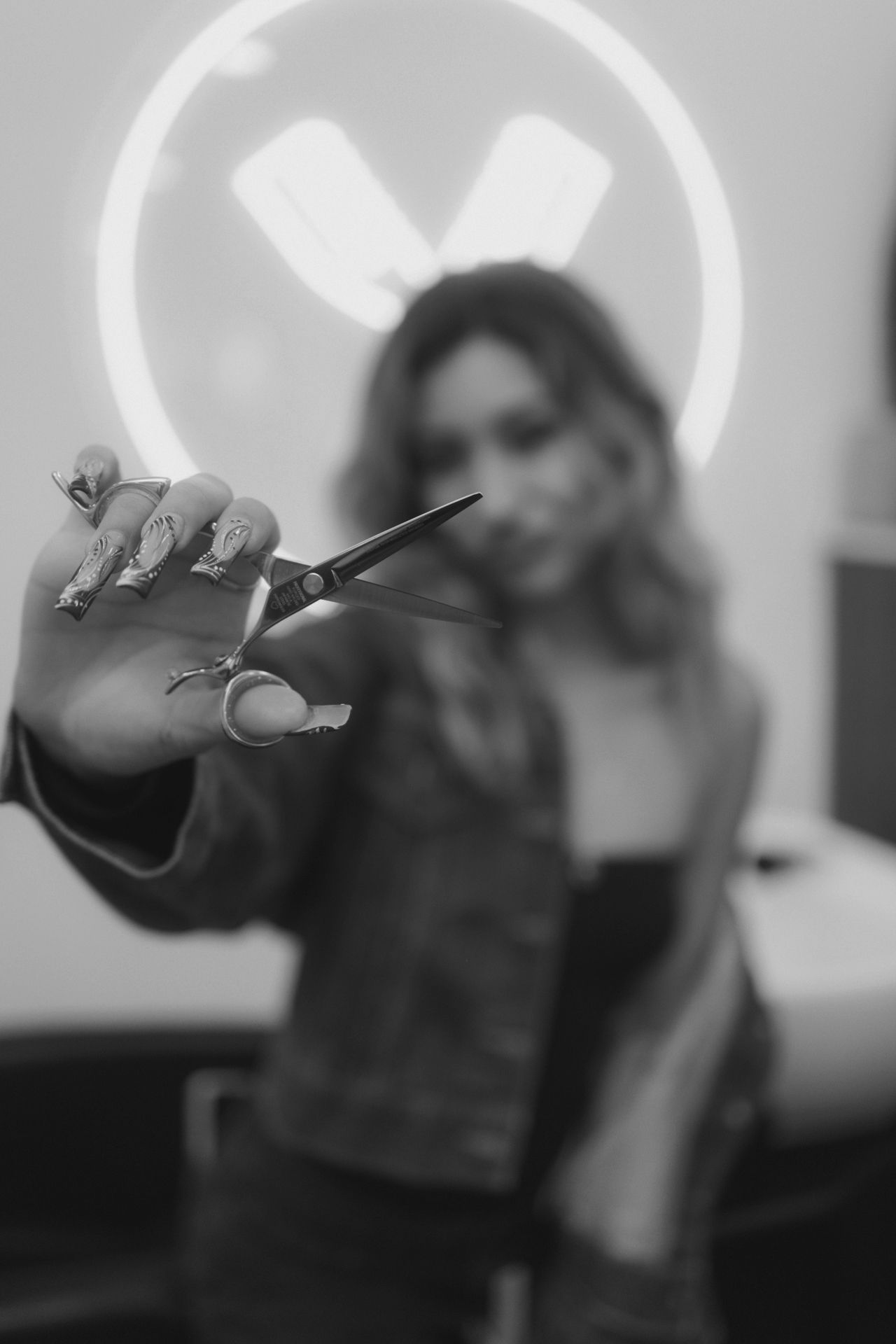 Artistic black and white photo of hands holding scissors with a backlit circular logo.