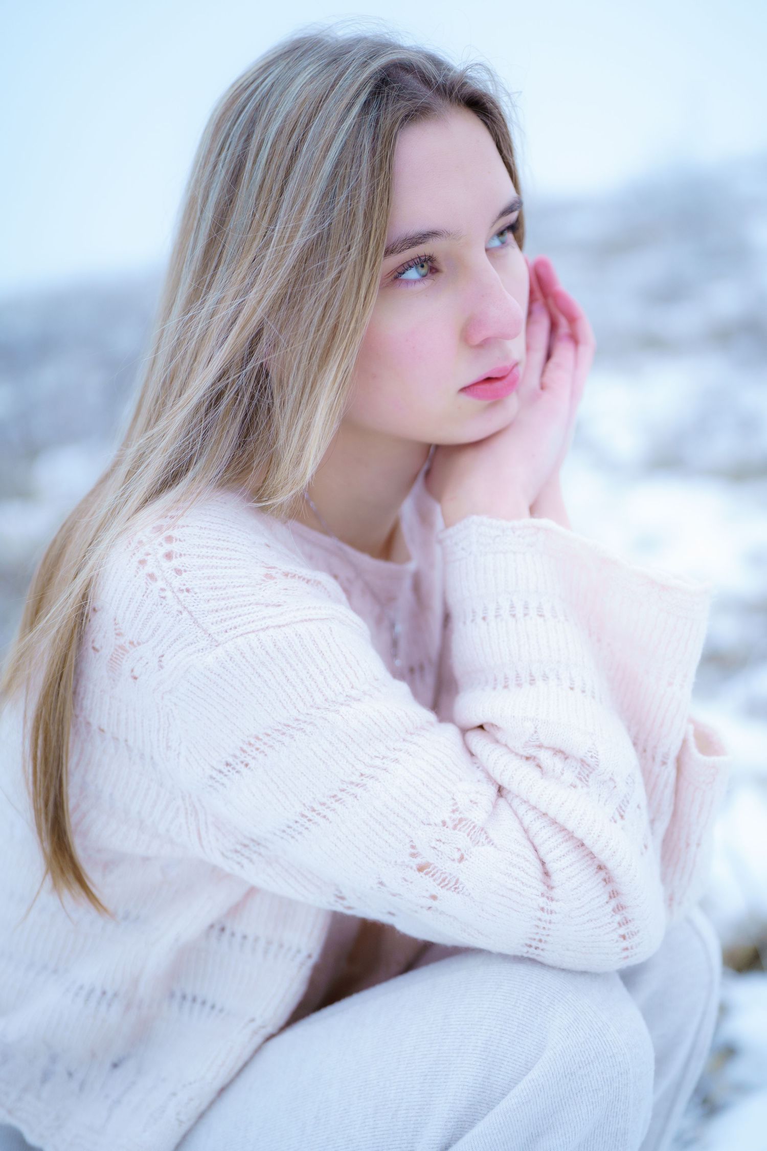 Figure in a white knit sweater poses thoughtfully in a snowy winter landscape with soft lighting.