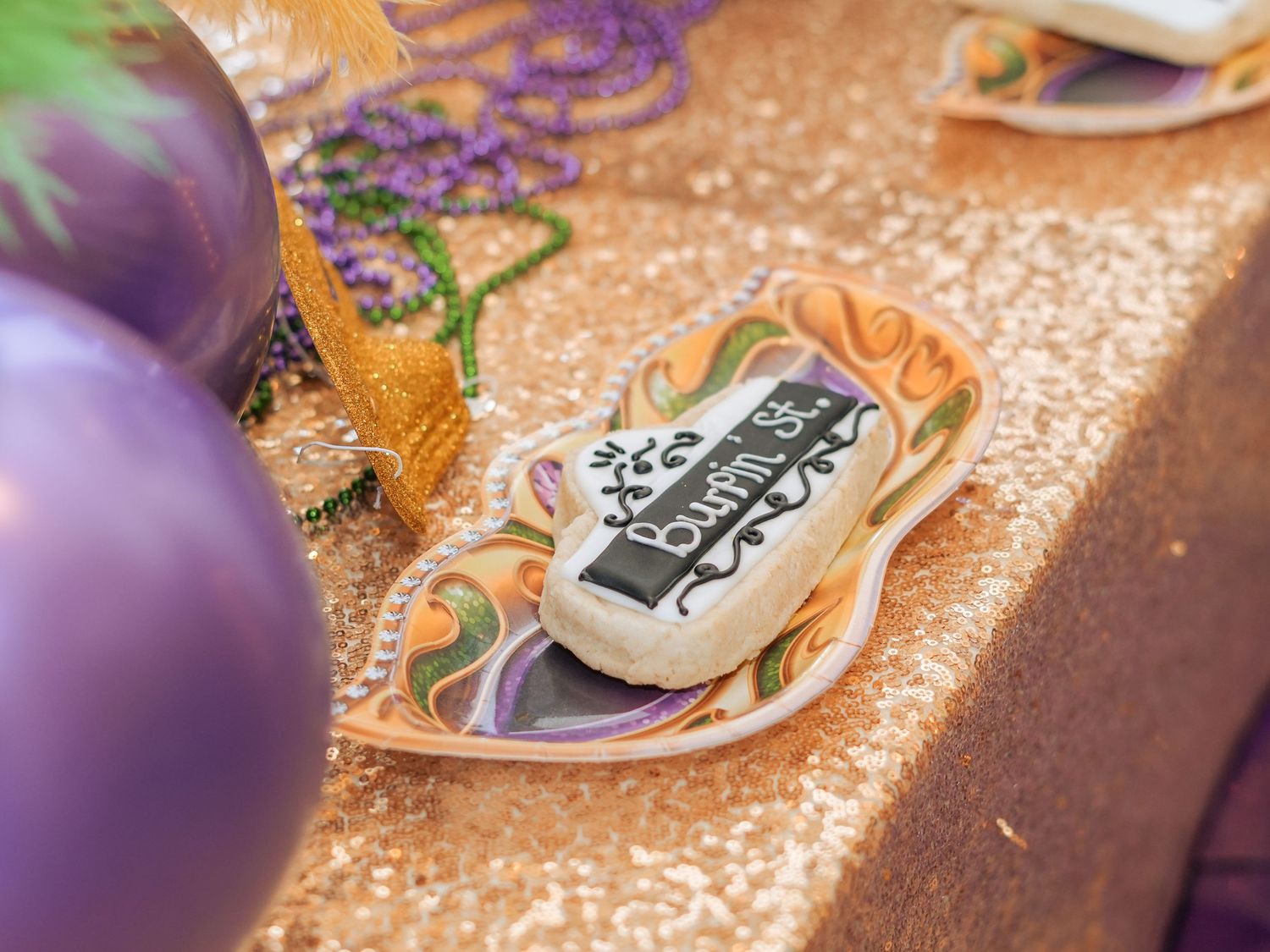 Close-up of a decorative birthday cookie on a sparkly gold tablecloth with purple accents.
