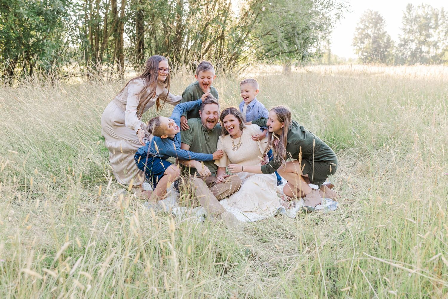 Large joyful family laughing together in a golden grass field during an outdoor photo session.