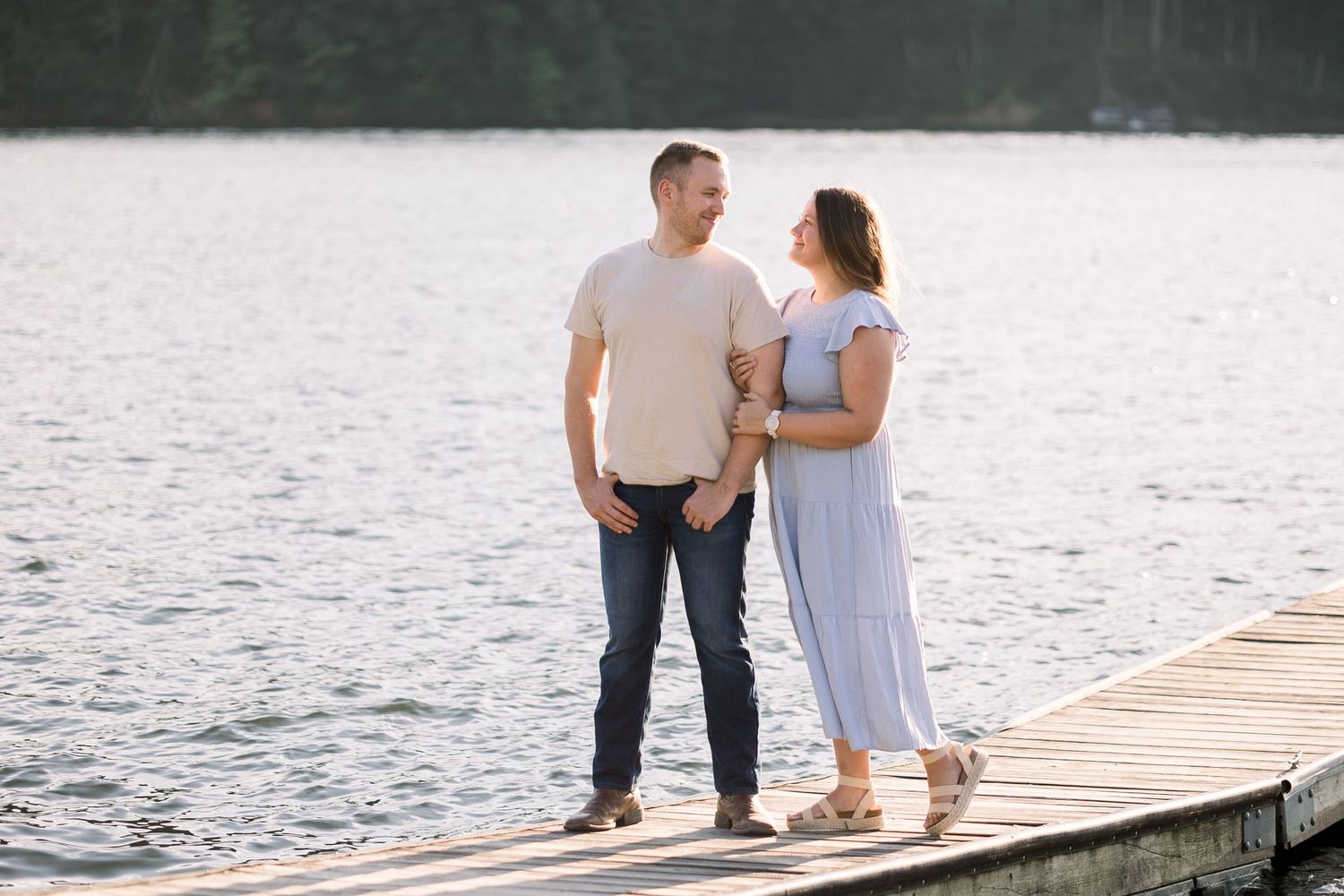 Couple walks hand in hand along a lakeside dock during a romantic photoshoot.