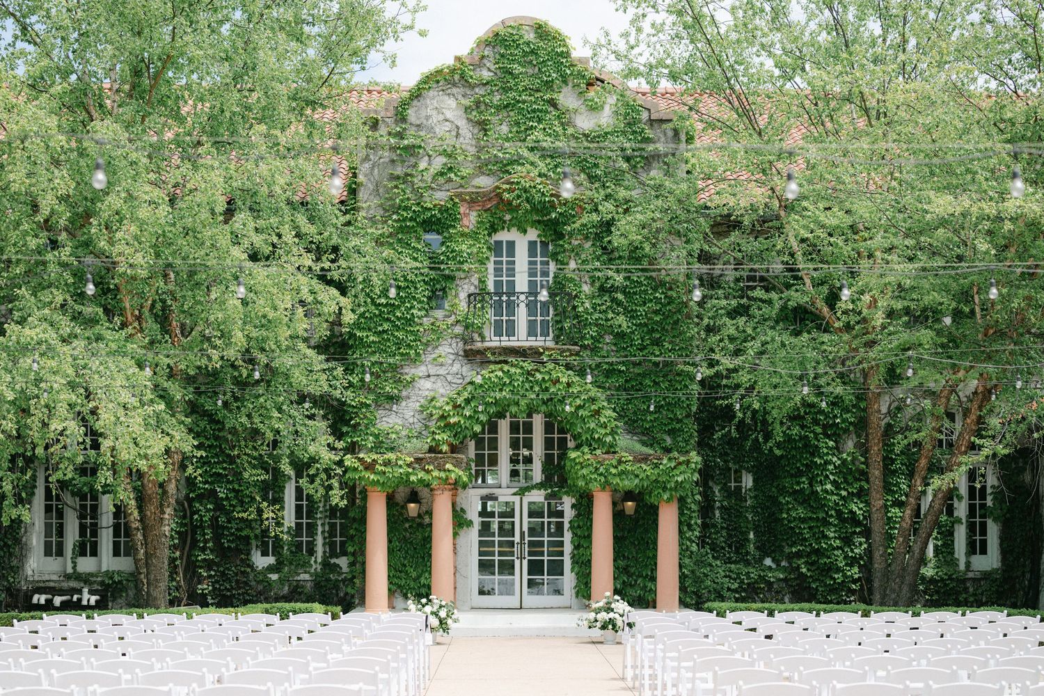 A person in a white wedding dress poses near a lush green garden archway covered in climbing vines.