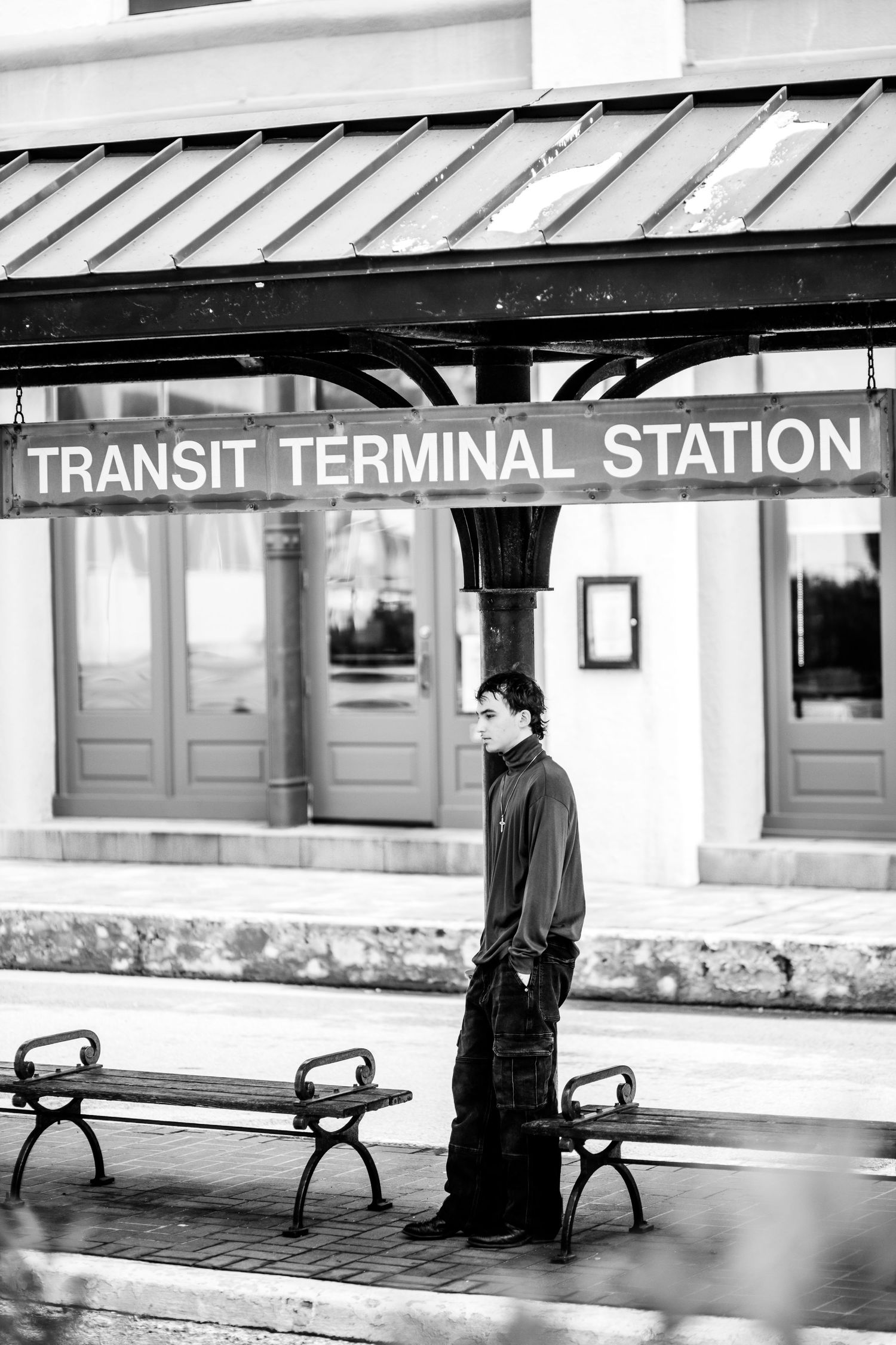 Black and white photograph of a transit terminal station platform with benches under a covered waiting area.