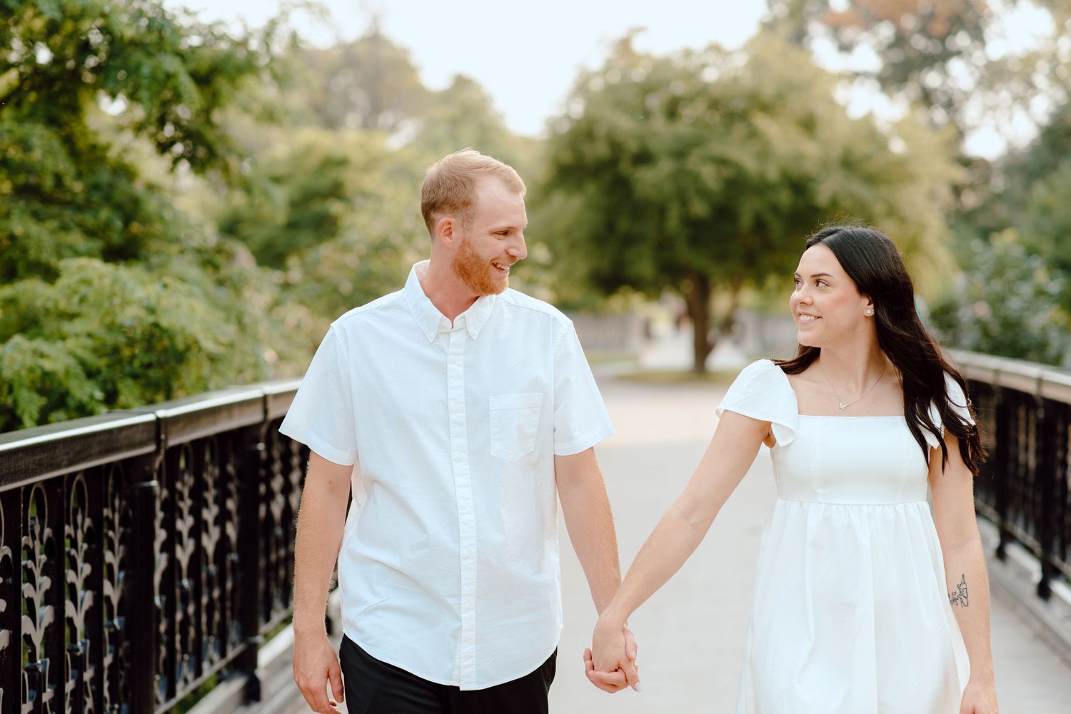 A couple shares a laugh while holding hands on a wooden bridge surrounded by greenery.