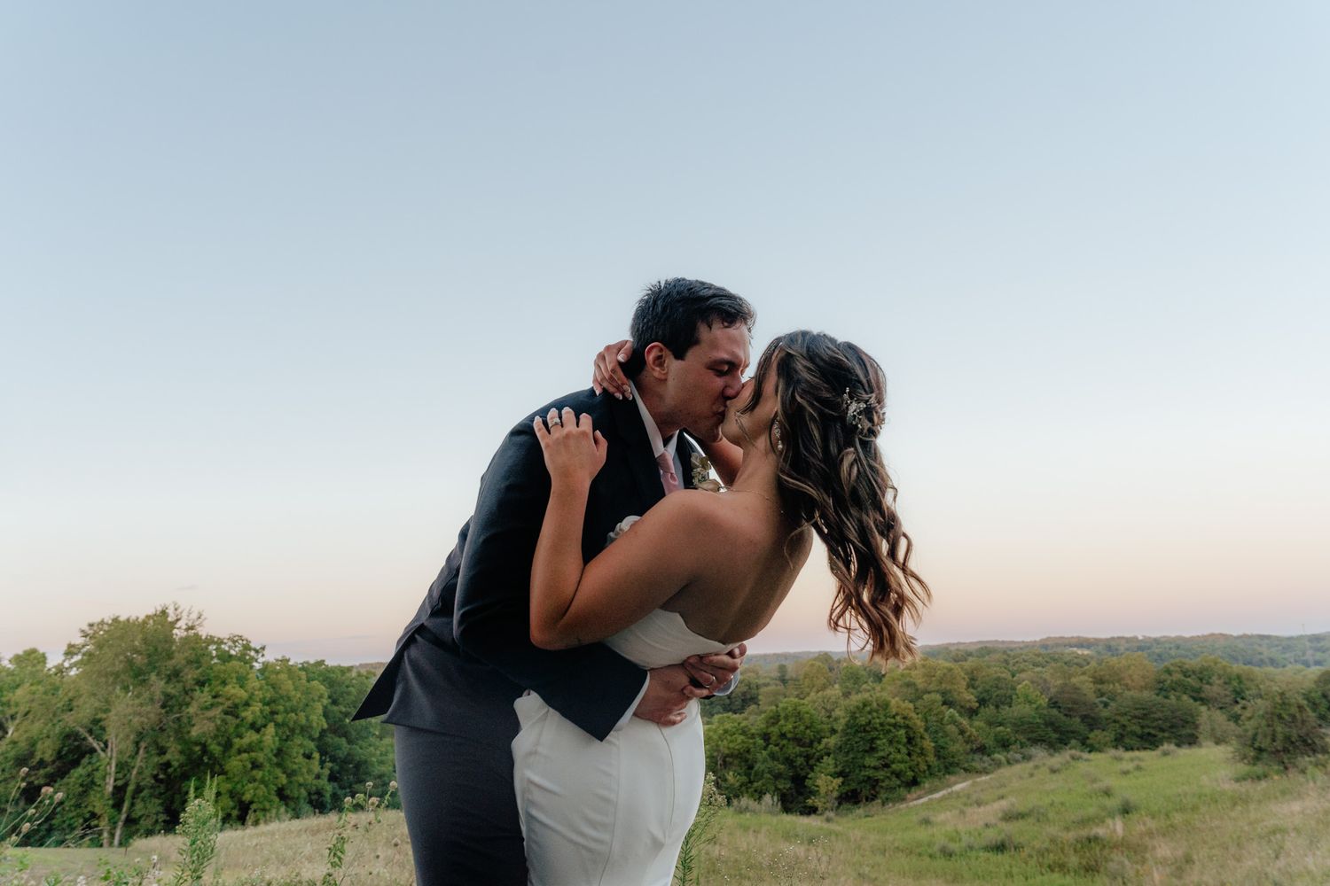 A romantic embrace between newlyweds on a hilltop at sunset with rolling hills in the background.