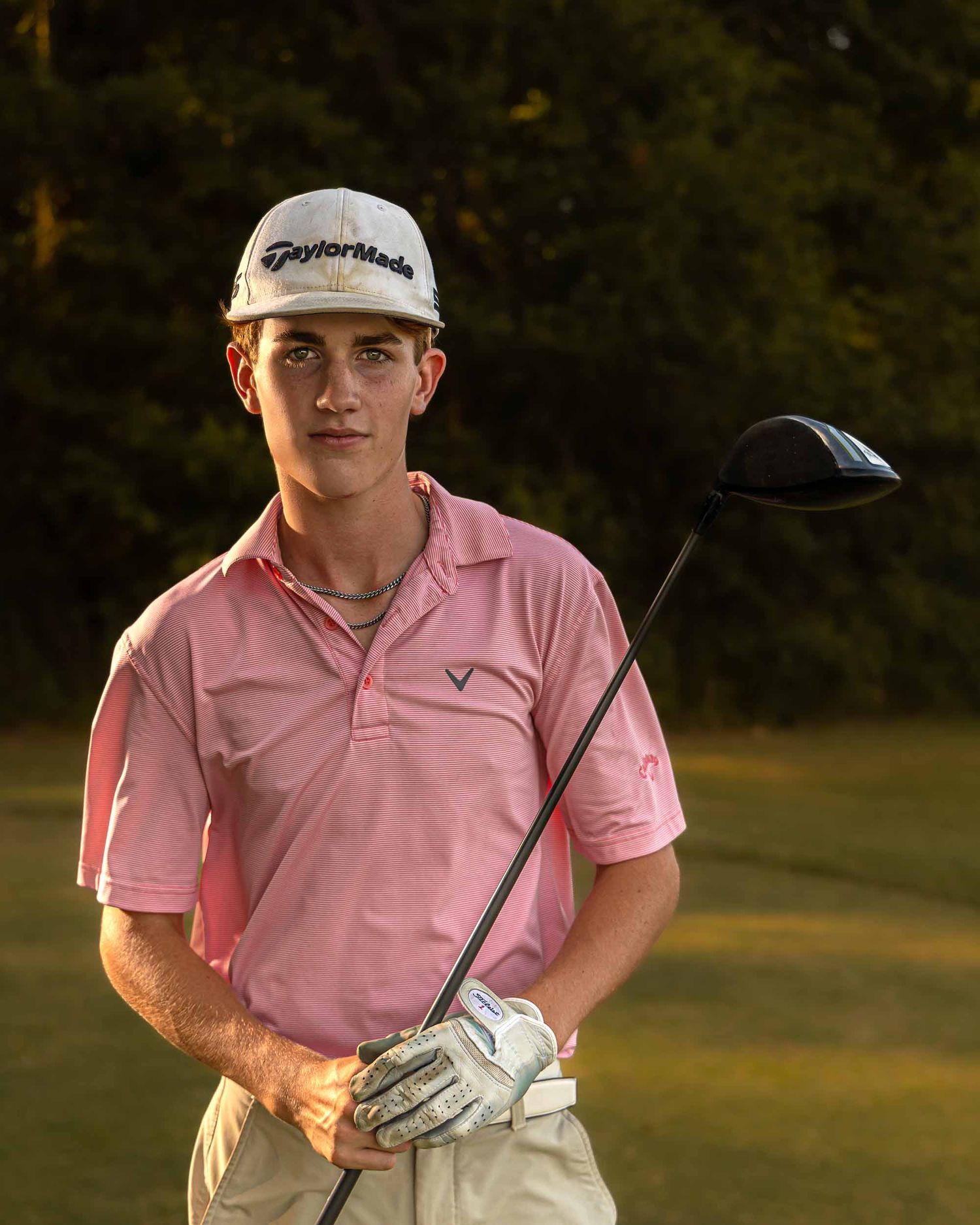 Golfer poses with club at sunset wearing pink polo and TaylorMade cap.