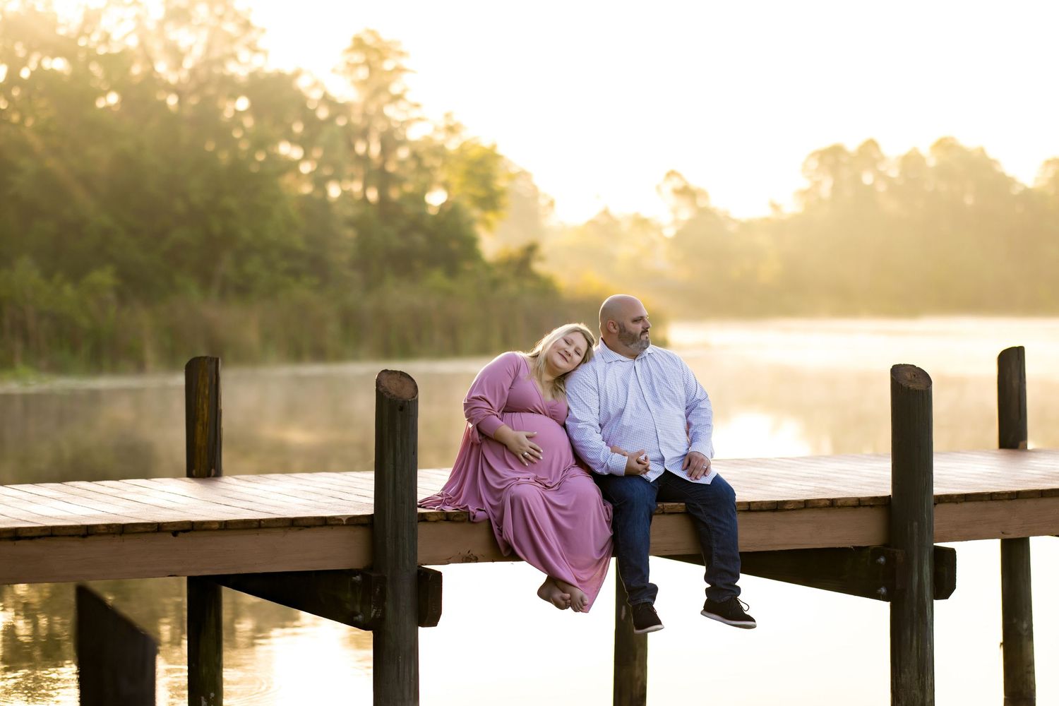 Couple sitting together on wooden dock at sunset overlooking peaceful lake.