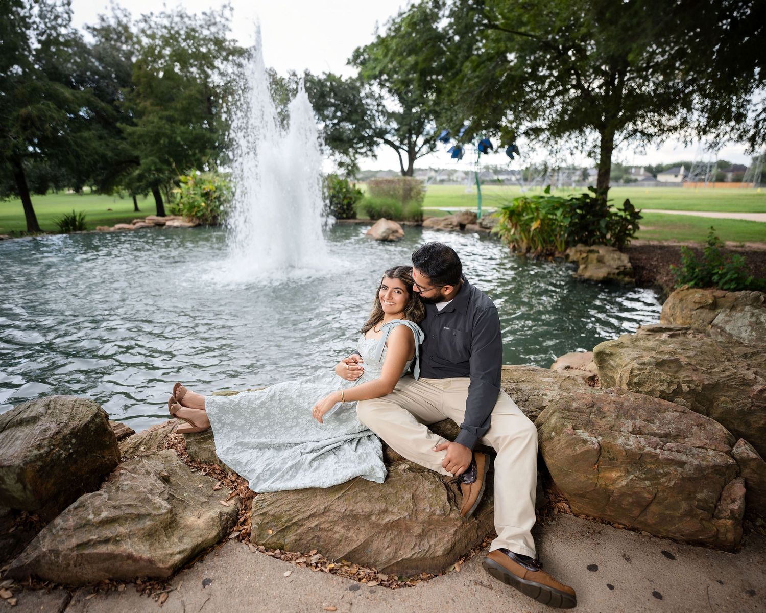 Couple sitting on rocks by fountain in landscaped garden setting.