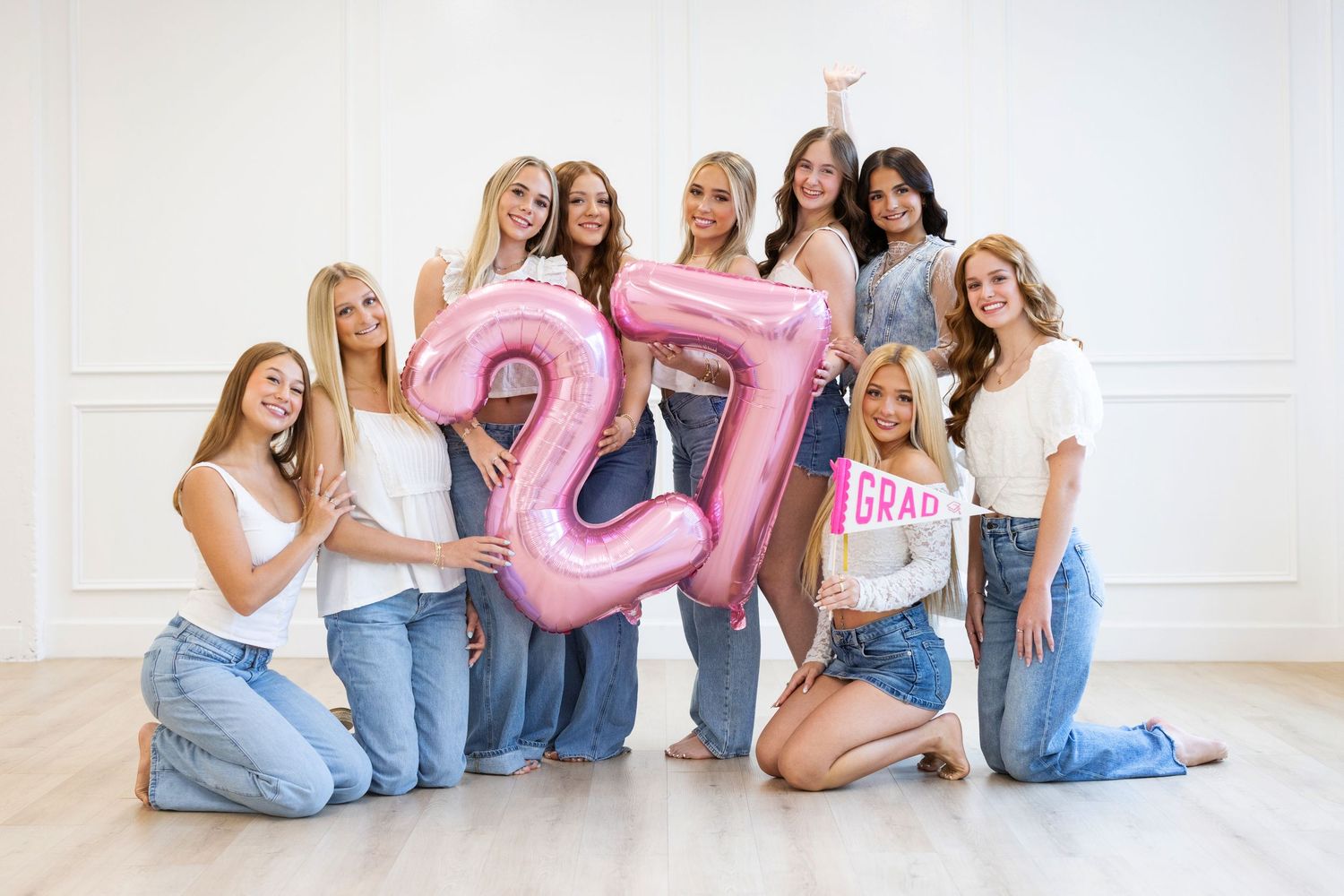 Group of 2027 high school graduates posing with pink number 27 balloons and celebrating graduation.