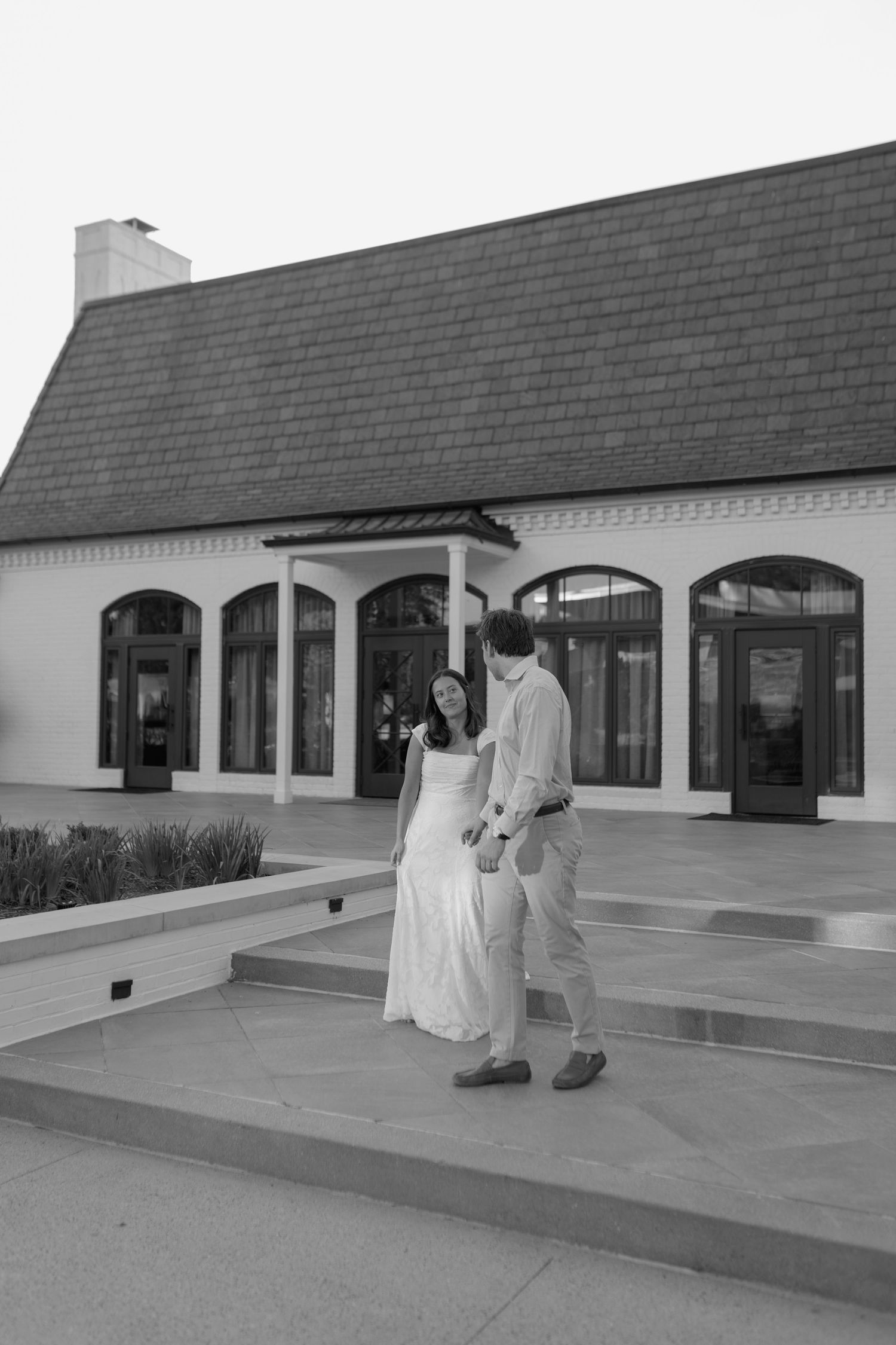 Black and white photo of a couple lying on grass, pointing at the sky on a sunny day.