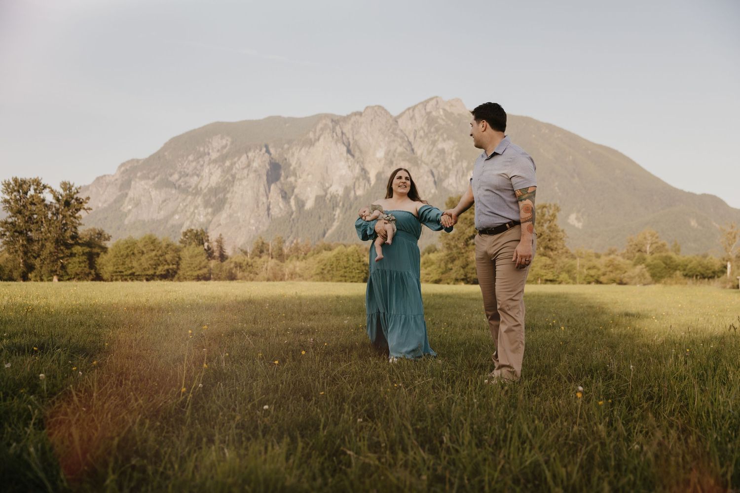 A couple walking in a meadow during golden hour for their newborn family session in North Bend, WA