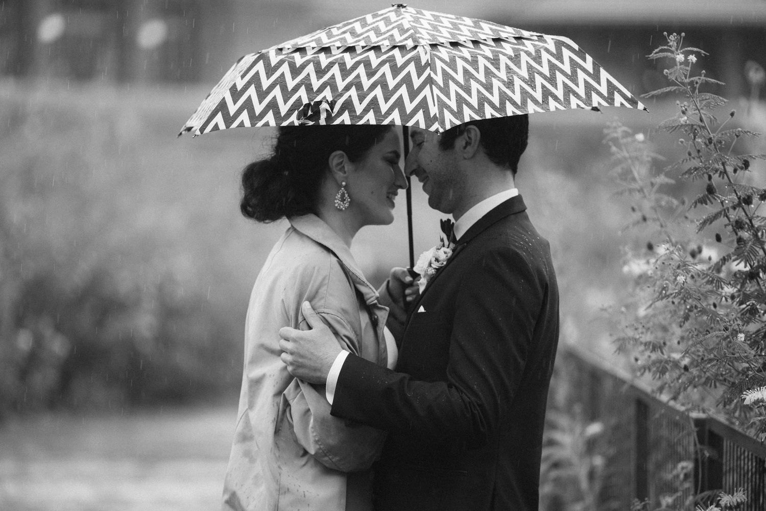 Black and white photo of a wedding couple kissing under a chevron umbrella in the rain, capturing a romantic wedding moment in Chicago