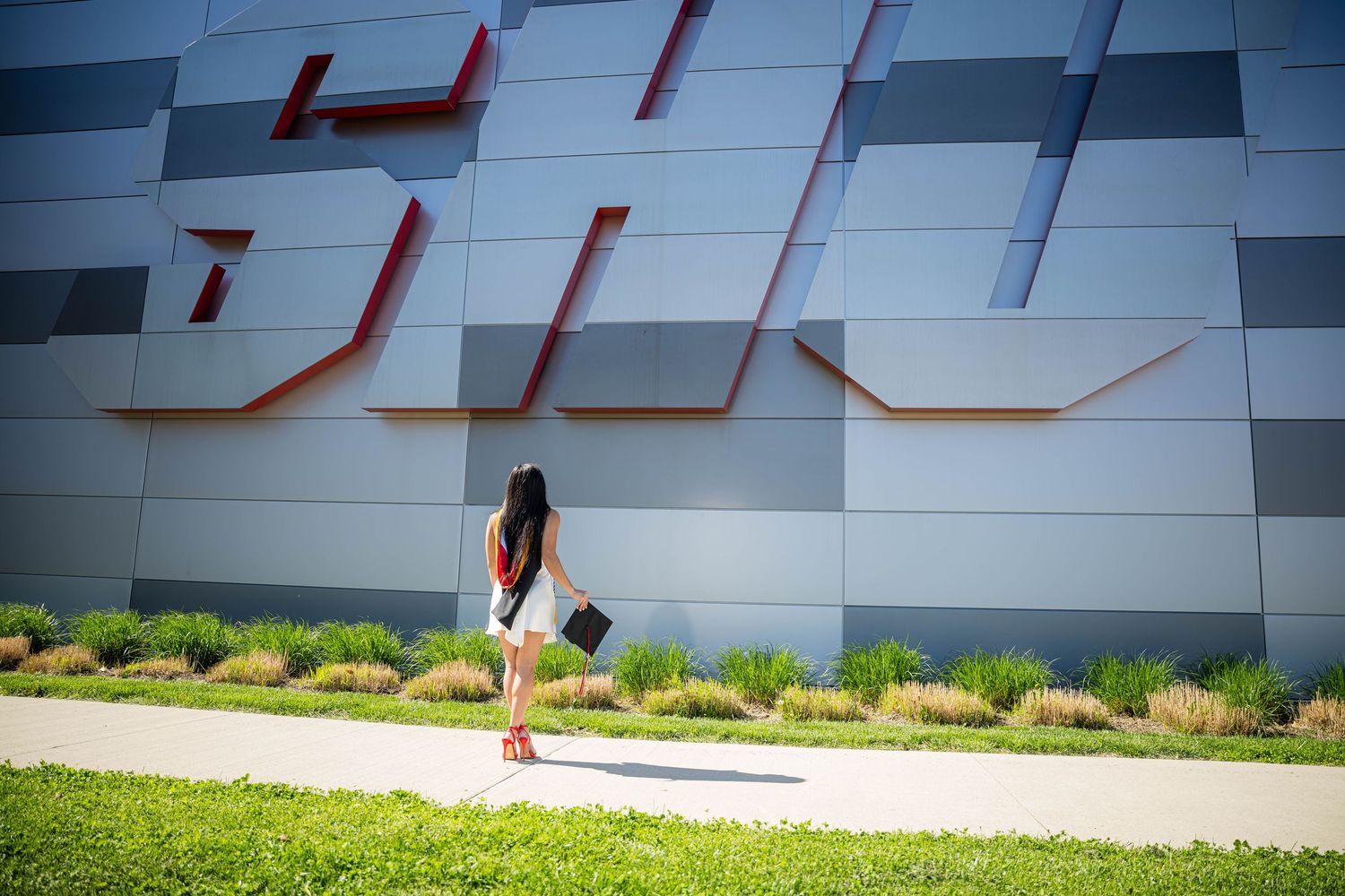 Woman walking past a modern building with large SIU letters on a sunny day.