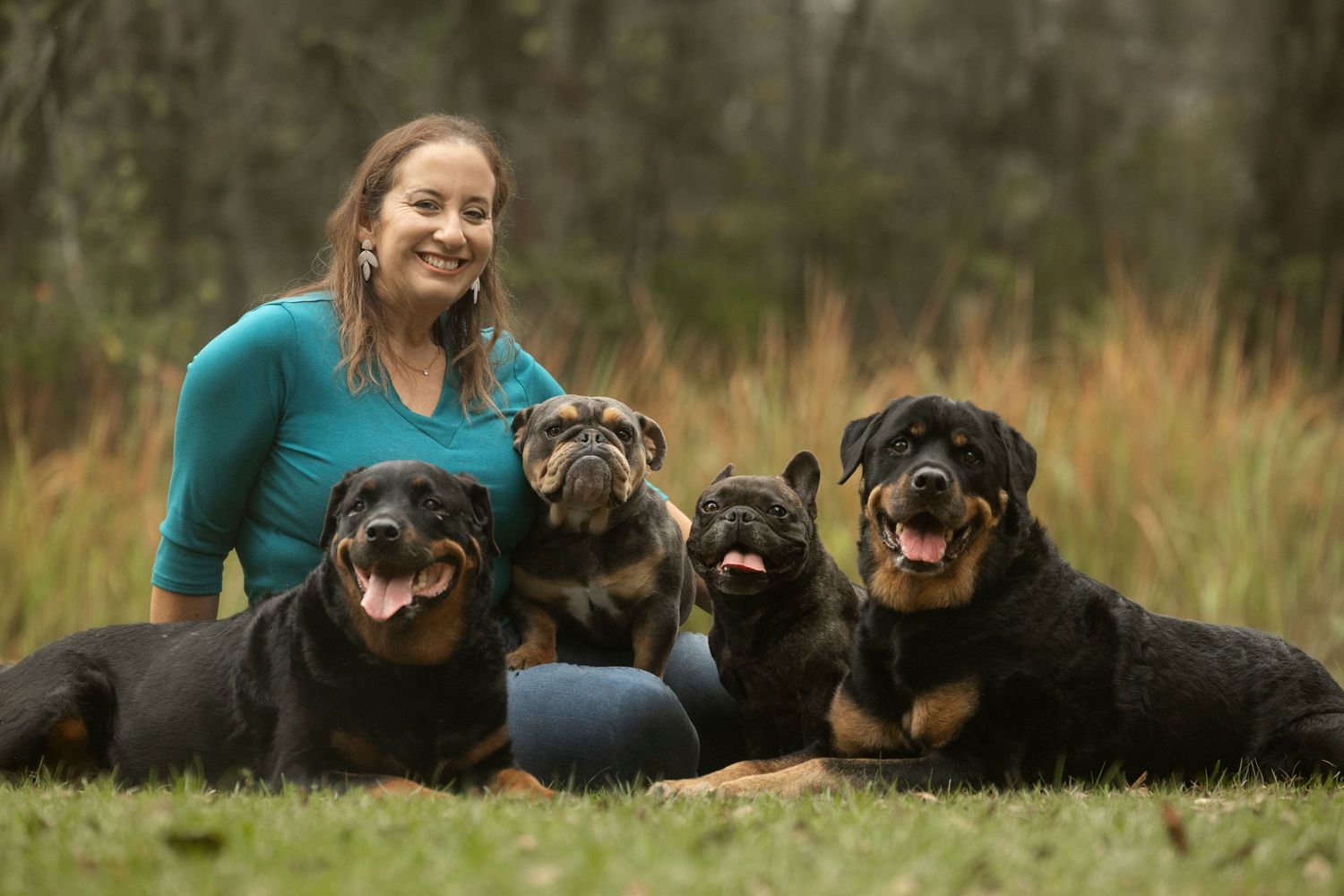A woman sitting in a grassy park surrounded by her four rescue dogs of various breeds.