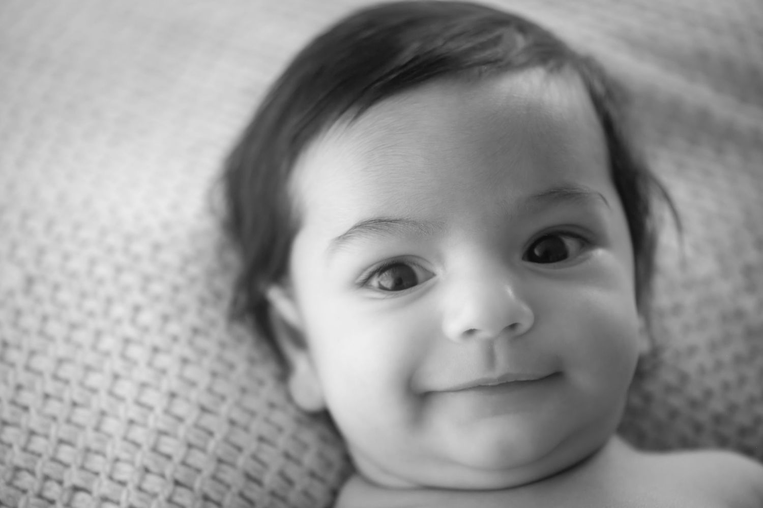 Black and white close-up portrait of a smiling baby lying on textured fabric.