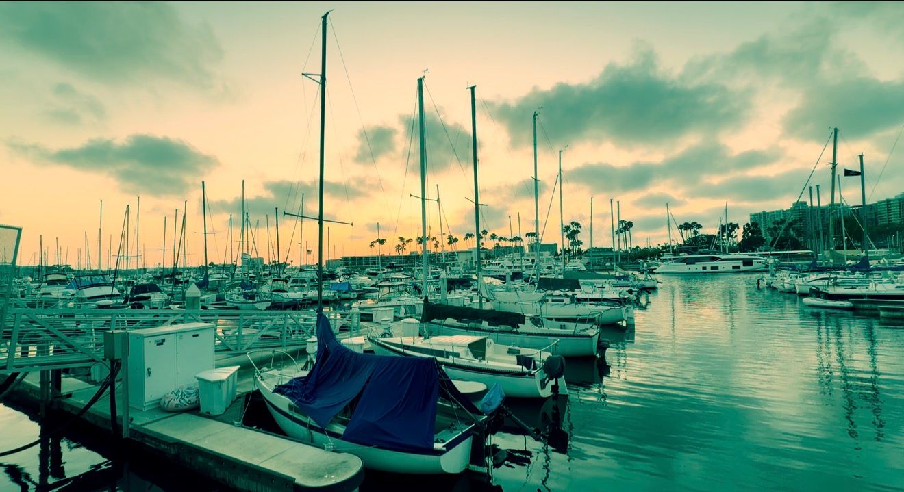 Sailboats docked in a marina at sunset with golden skies and calm water reflections.