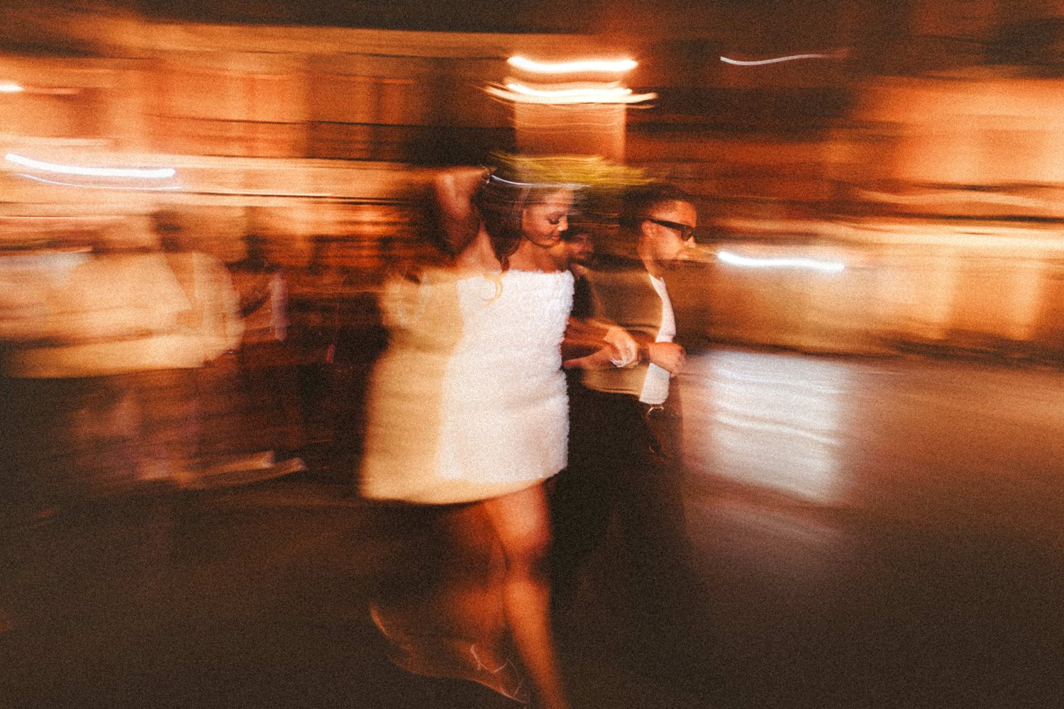 Blurry motion shot of couple dancing at a wedding reception with warm glowing lights in background.