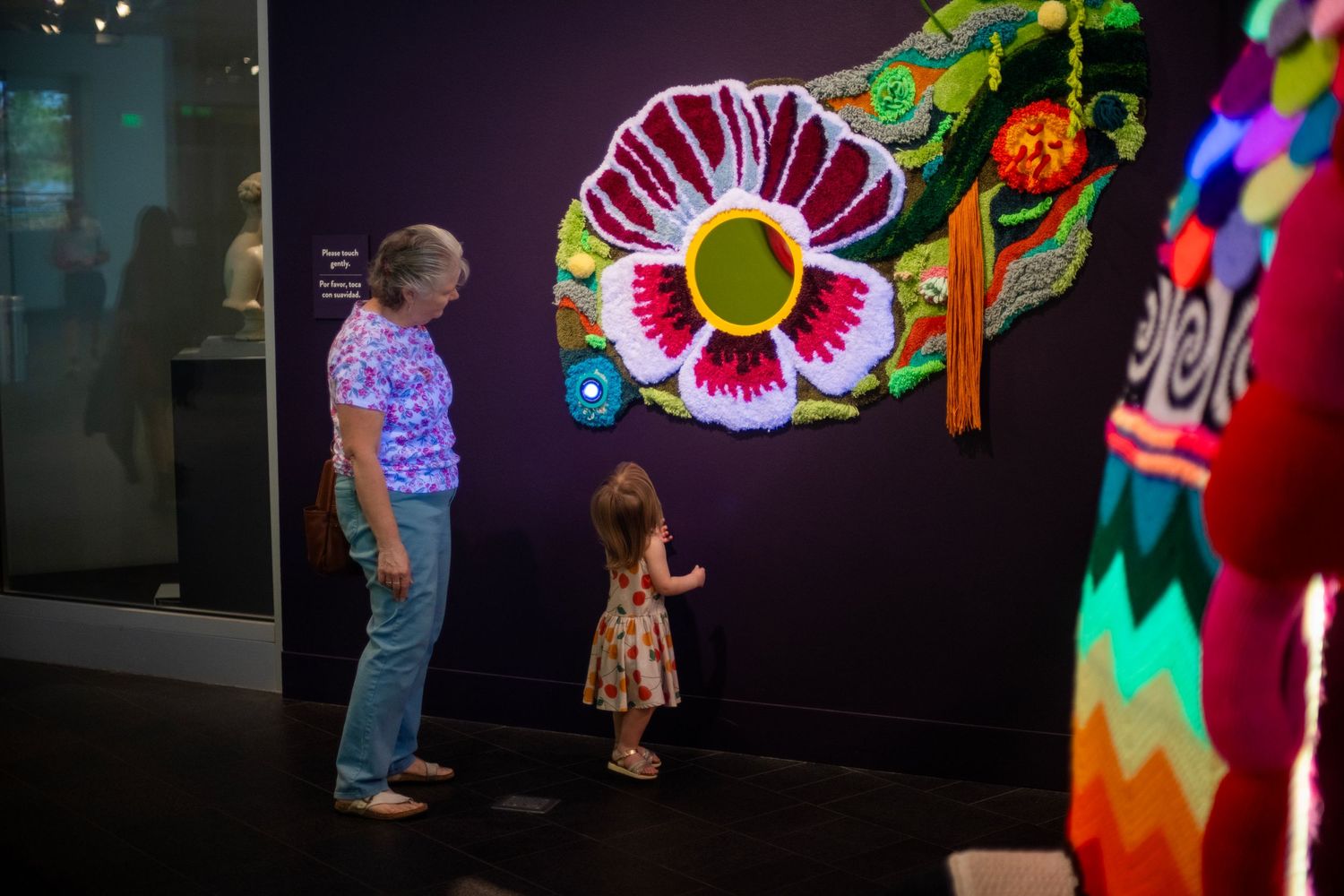 Adult and child admiring colorful floral folk art wall sculpture in a dimly lit museum gallery.