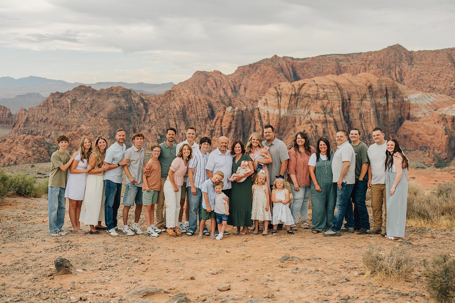 Large family group portrait outdoors at Snow Canyon State Park with stunning red rock formations in the background.