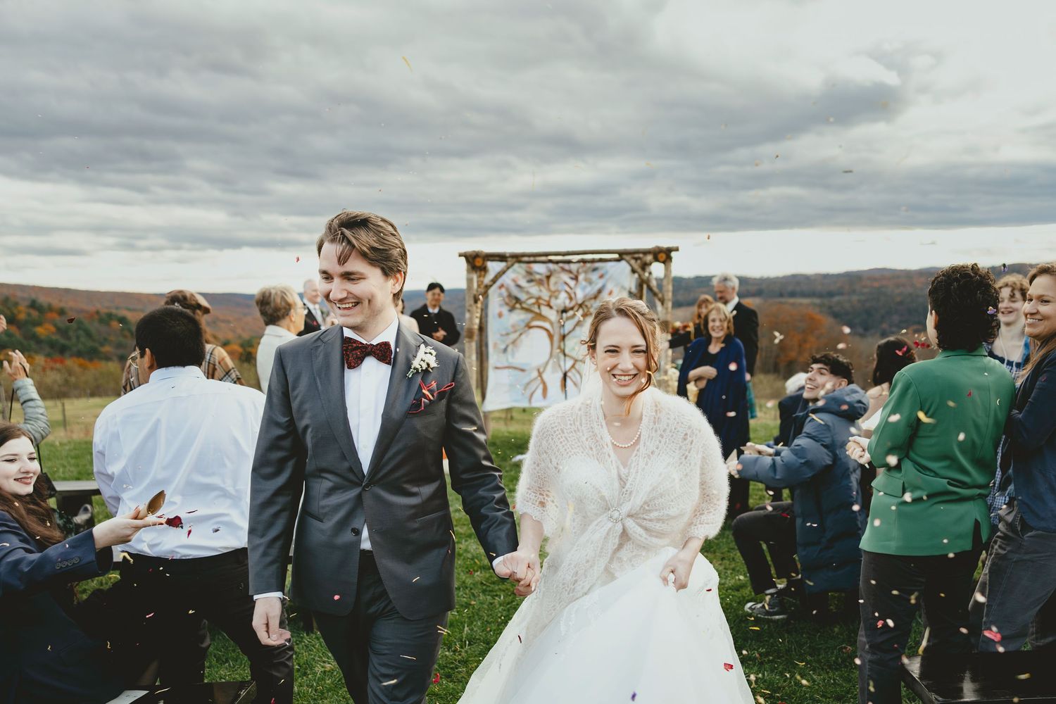 A couple stands on a snowy beach during their winter wedding with mountains and water in the background.
