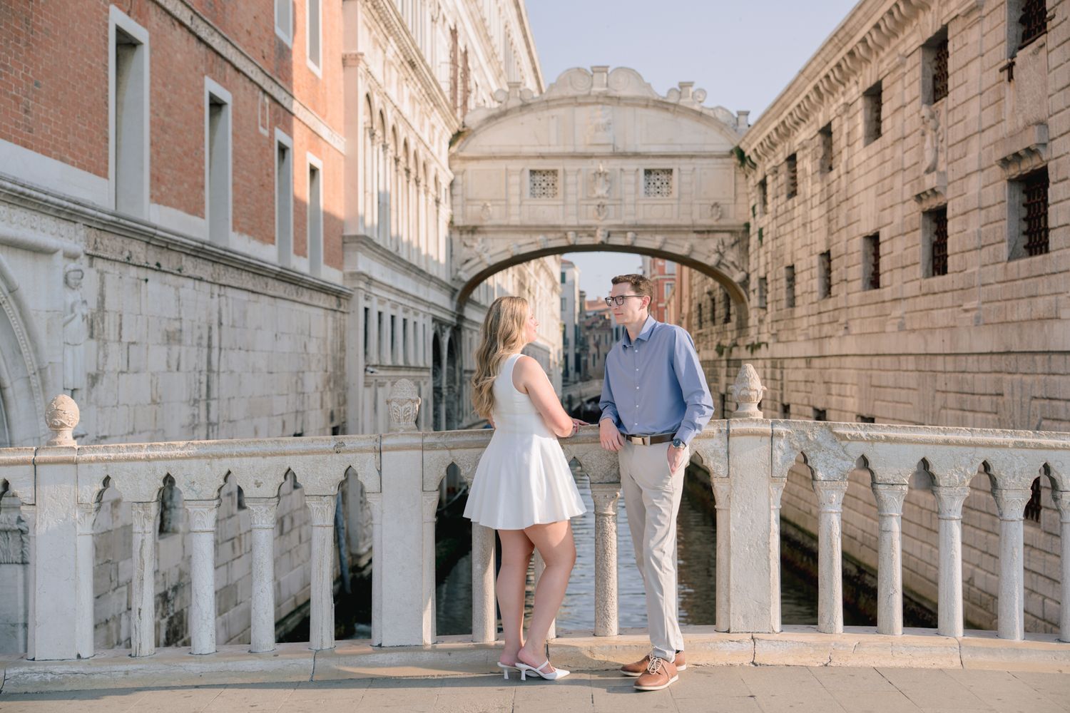 Couple holding hands in front of the Bridge of Sighs in Venice, Italy on a sunny day.