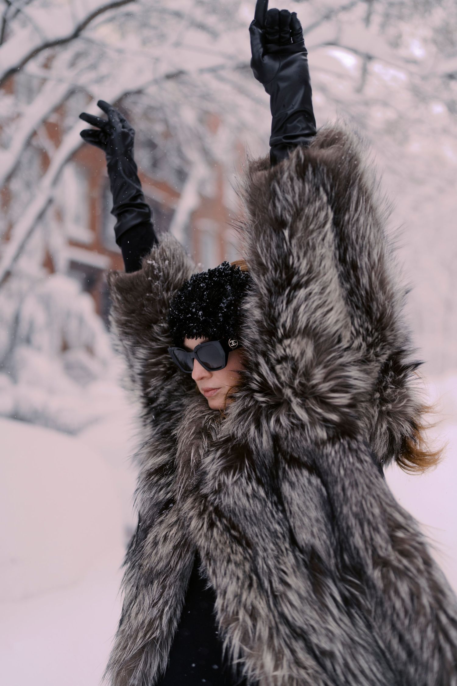 Person in a luxurious gray fur coat poses dramatically against a snowy winter backdrop.