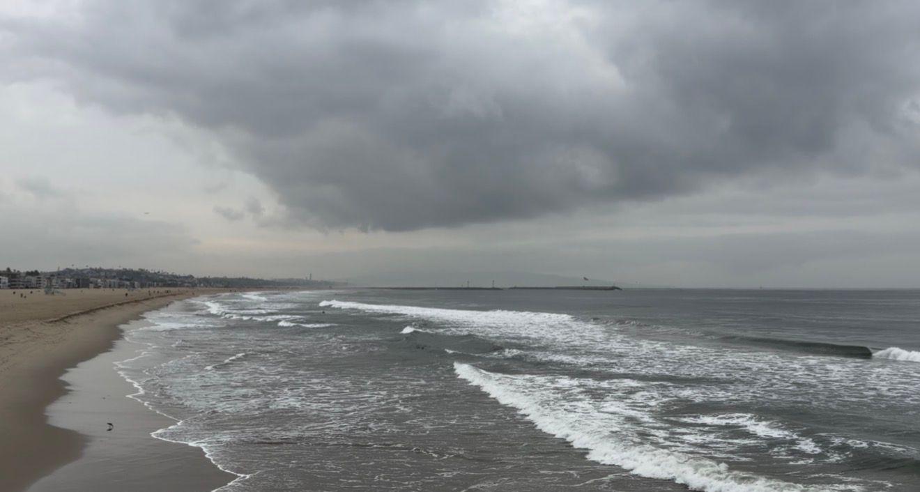 Dramatic panoramic view of a stormy coastline with crashing waves and dark cloudy skies over a sandy beach.