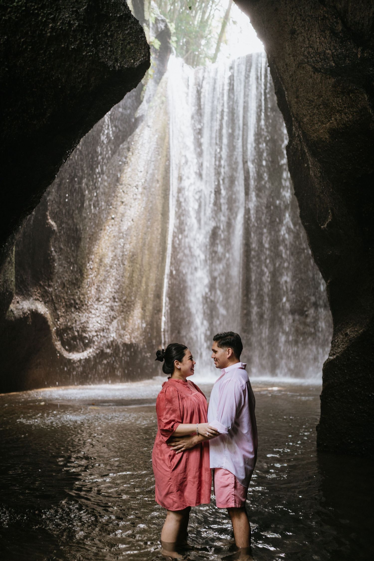 A romantic moment by a majestic waterfall in a natural cave setting.