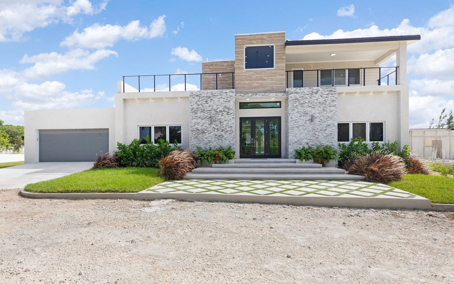 Modern white stone and glass house exterior with landscaped yard and gravel driveway showcases contemporary architecture.
