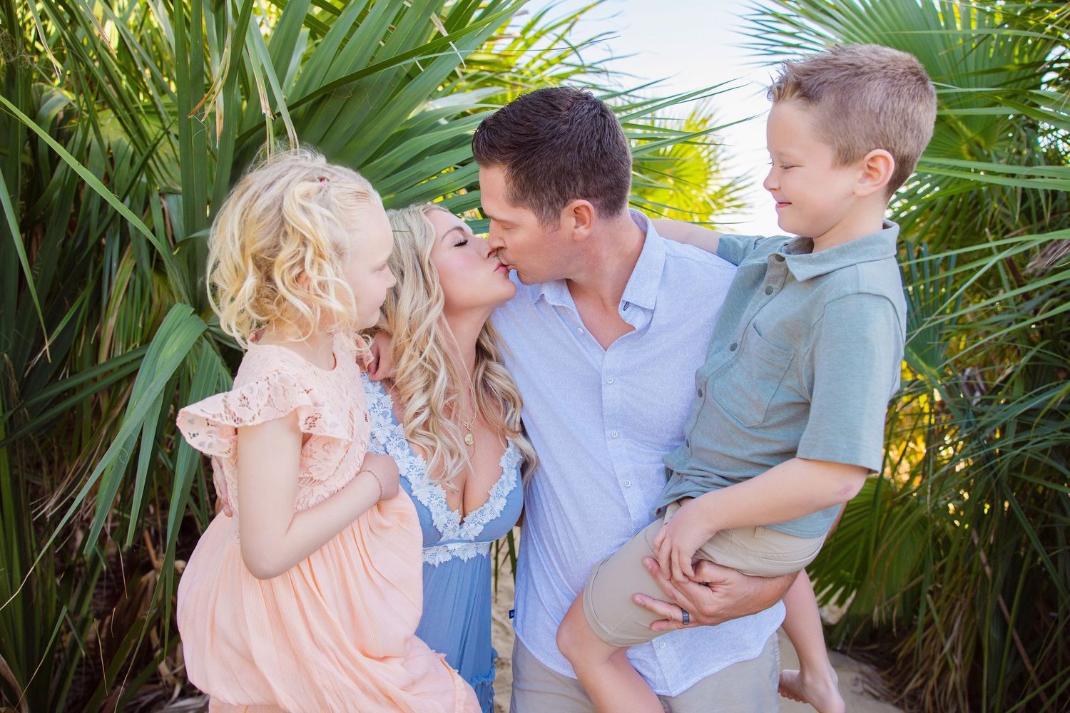 A family wearing white outfits shares a playful moment together on a sandy beach.