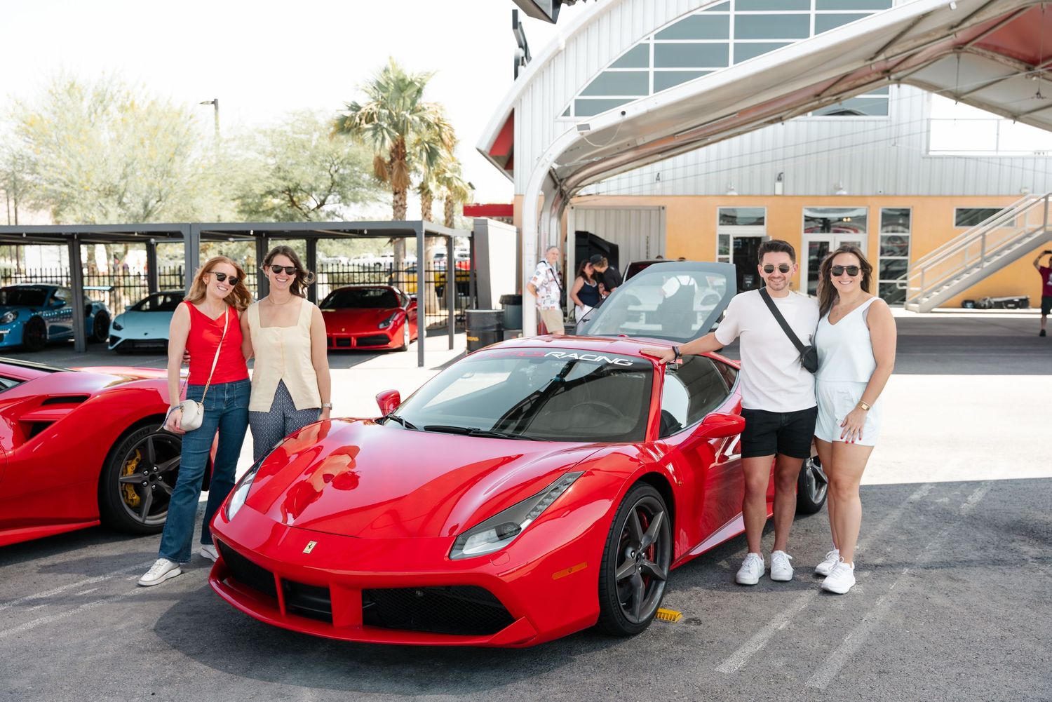 A row of red Ferrari sports cars parked at a dealership showroom with customers viewing the vehicles.