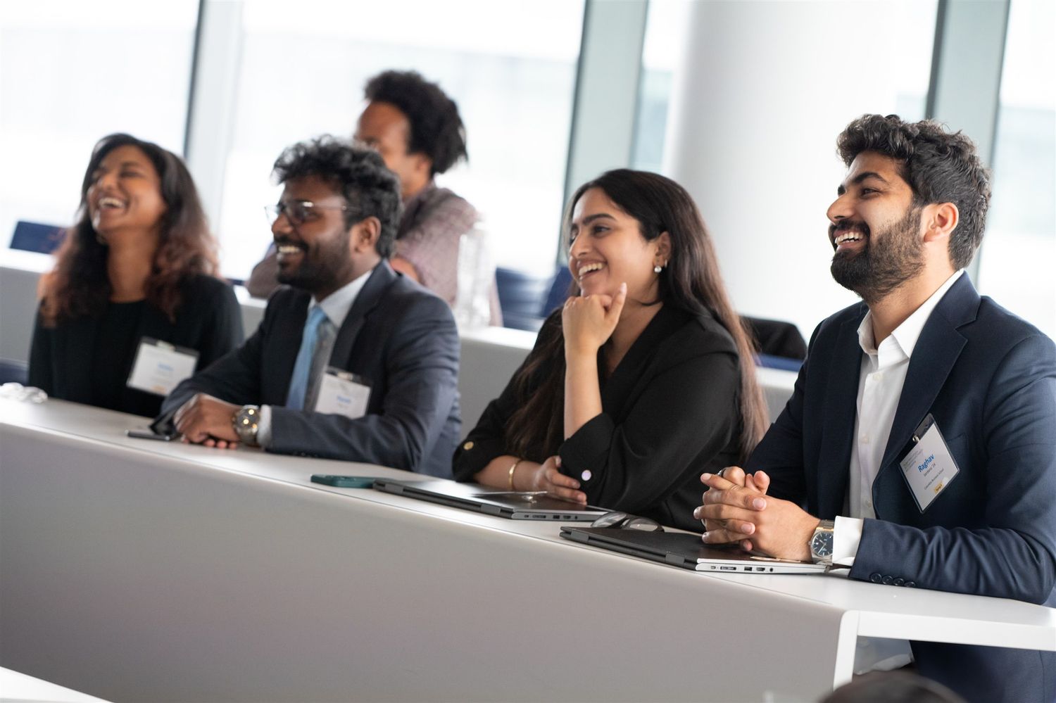 Business professionals laugh together during a meeting in a bright modern conference room.