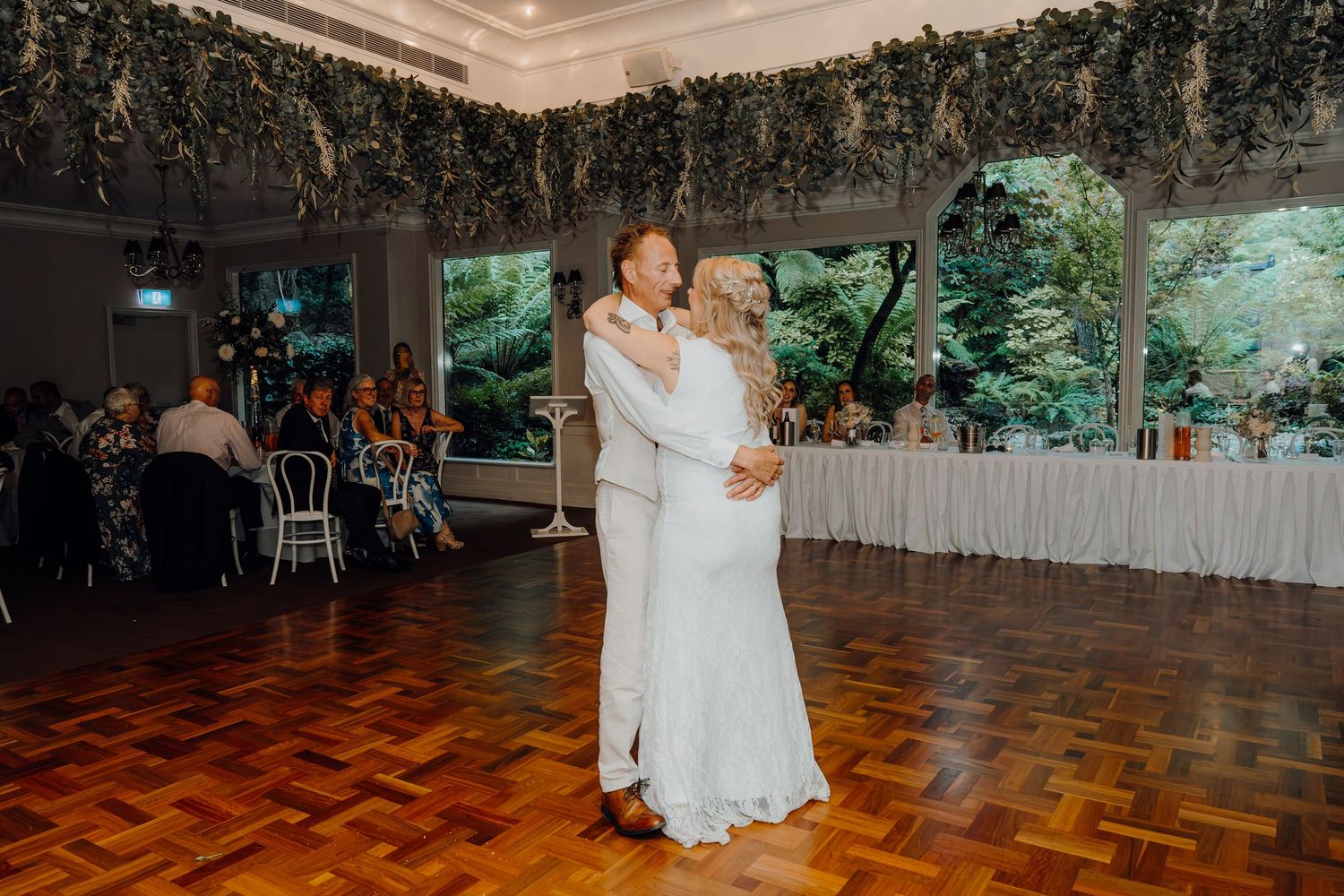 Elegantly decorated wedding reception venue with parquet dance floor and greenery-covered walls and ceiling.